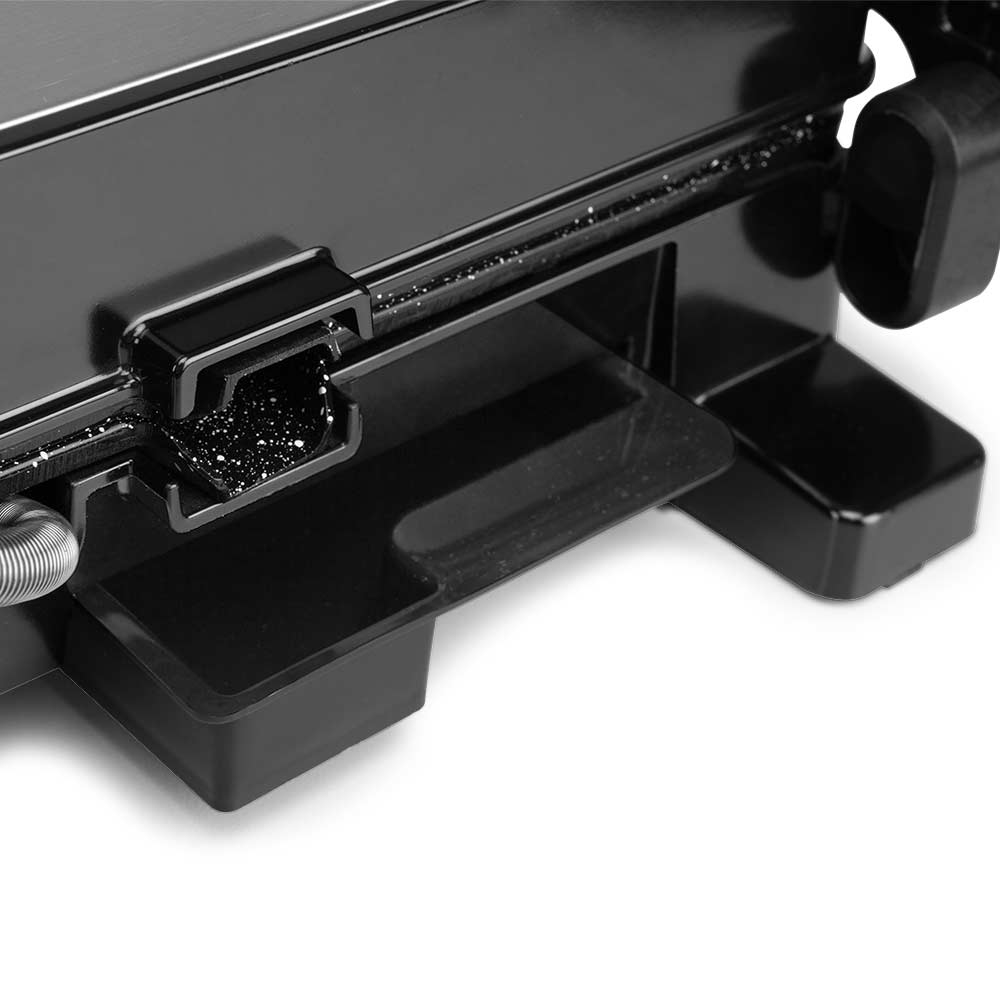 Primo piano di un elettrodomestico nero, che mostra un cassetto e parte di una superficie metallica con alcuni detriti.