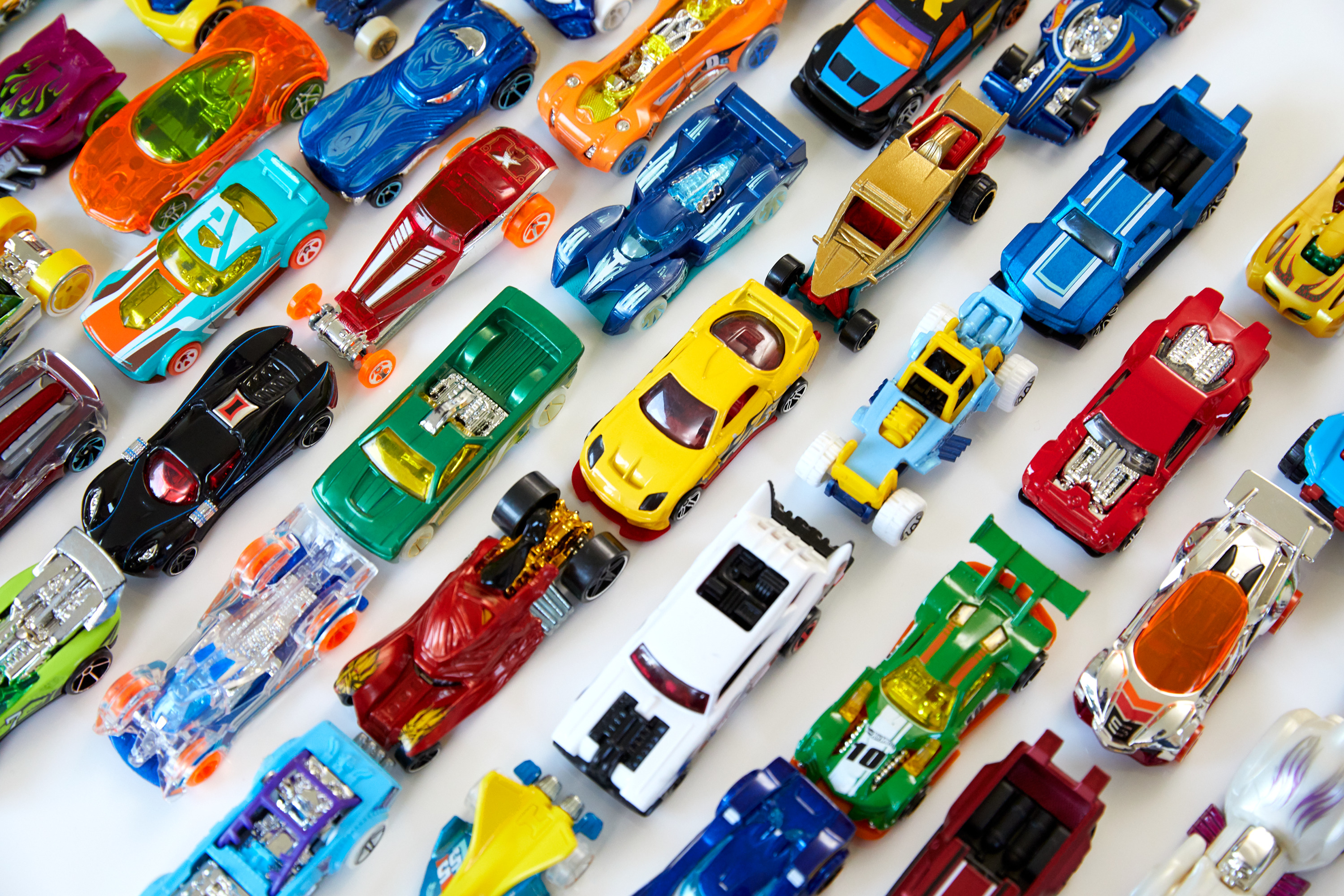 Sammlung von Hot Wheels Spielzeugautos, verschiedene Farben und Designs, eng aneinandergereiht auf weißem Untergrund.
