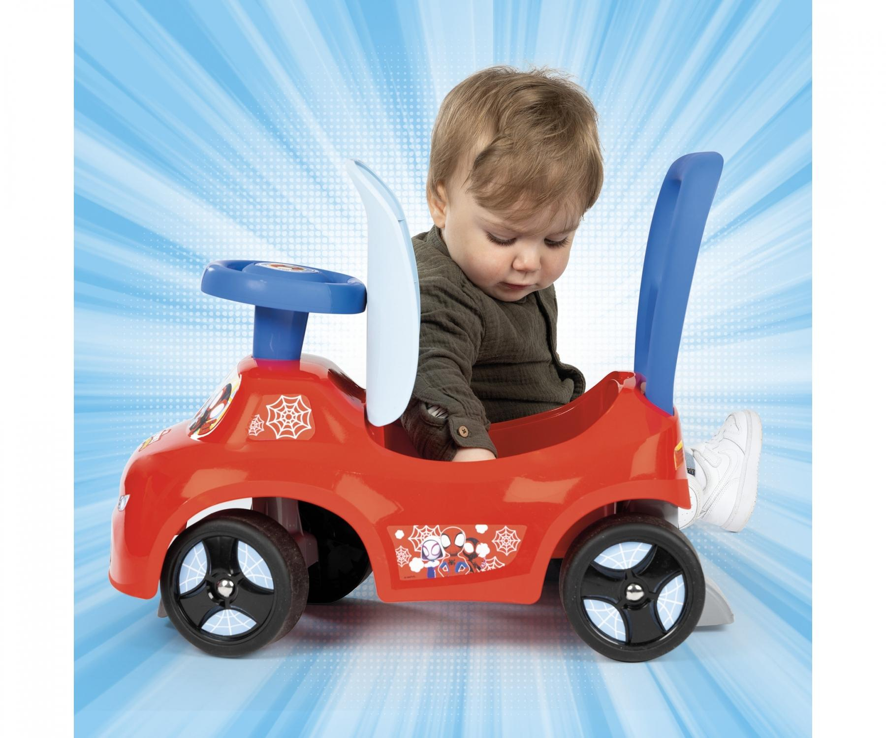 Ein Kleinkind sitzt in einem roten Spielzeugauto mit einem blauen Schiebegriff.