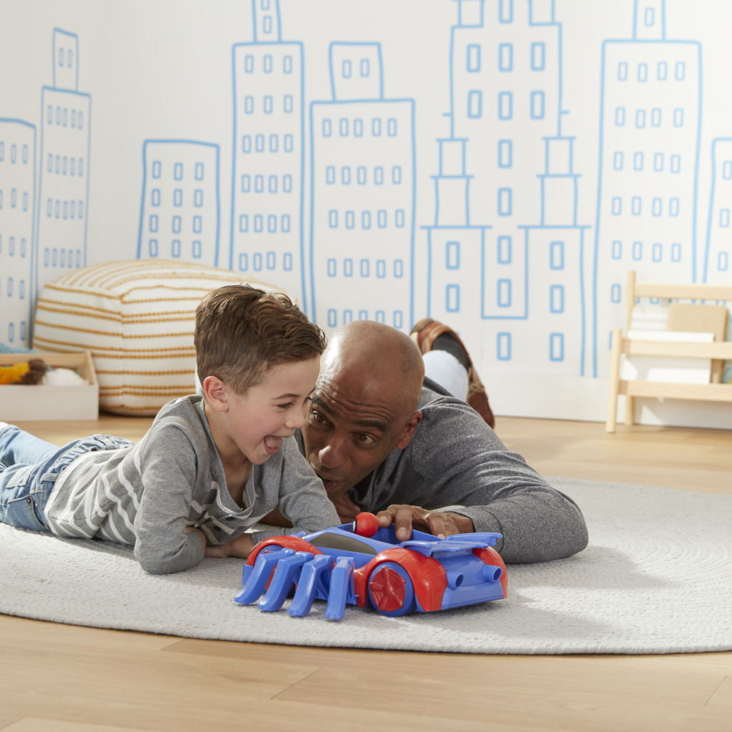 Ojciec i syn bawią się zabawką samochodu Spider-Mana na dywanie, uśmiechając się, w pokoju.