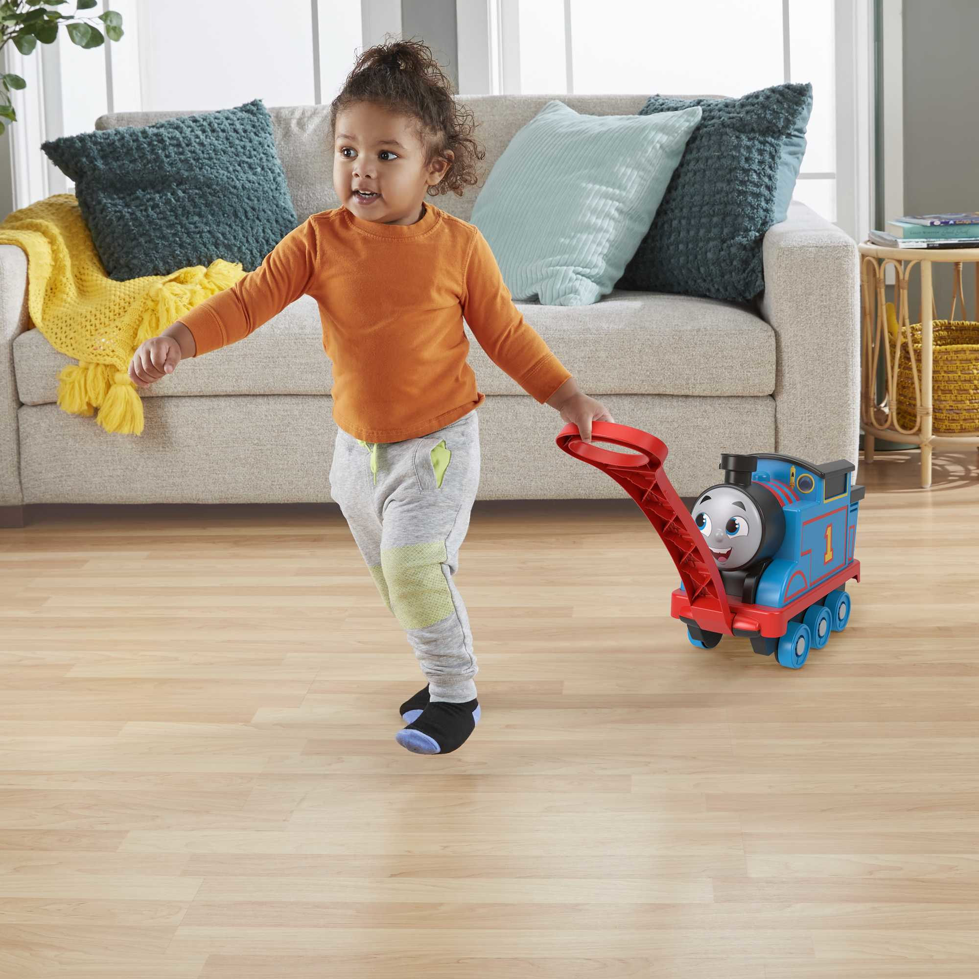 Kind zieht einen blauen Thomas die Lokomotive Spielzeugzug auf einem Holzboden. Ein Sofa ist im Hintergrund.