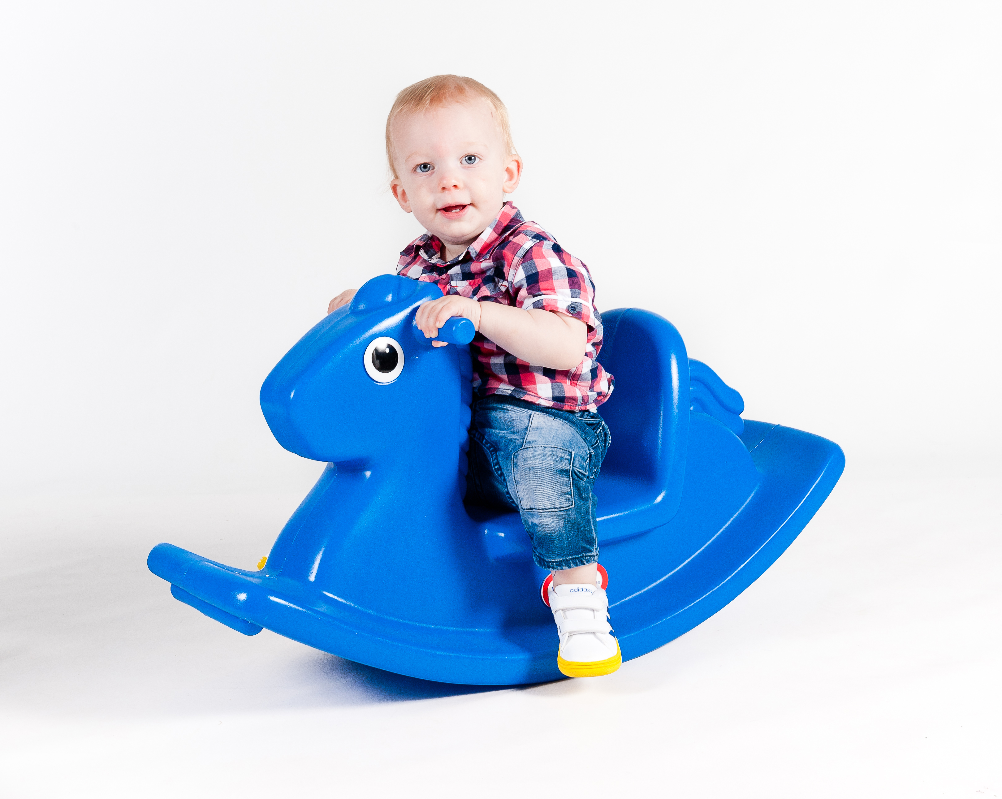 Un bambino piccolo su un cavallo a dondolo blu. Il bambino indossa una camicia a quadri e jeans.