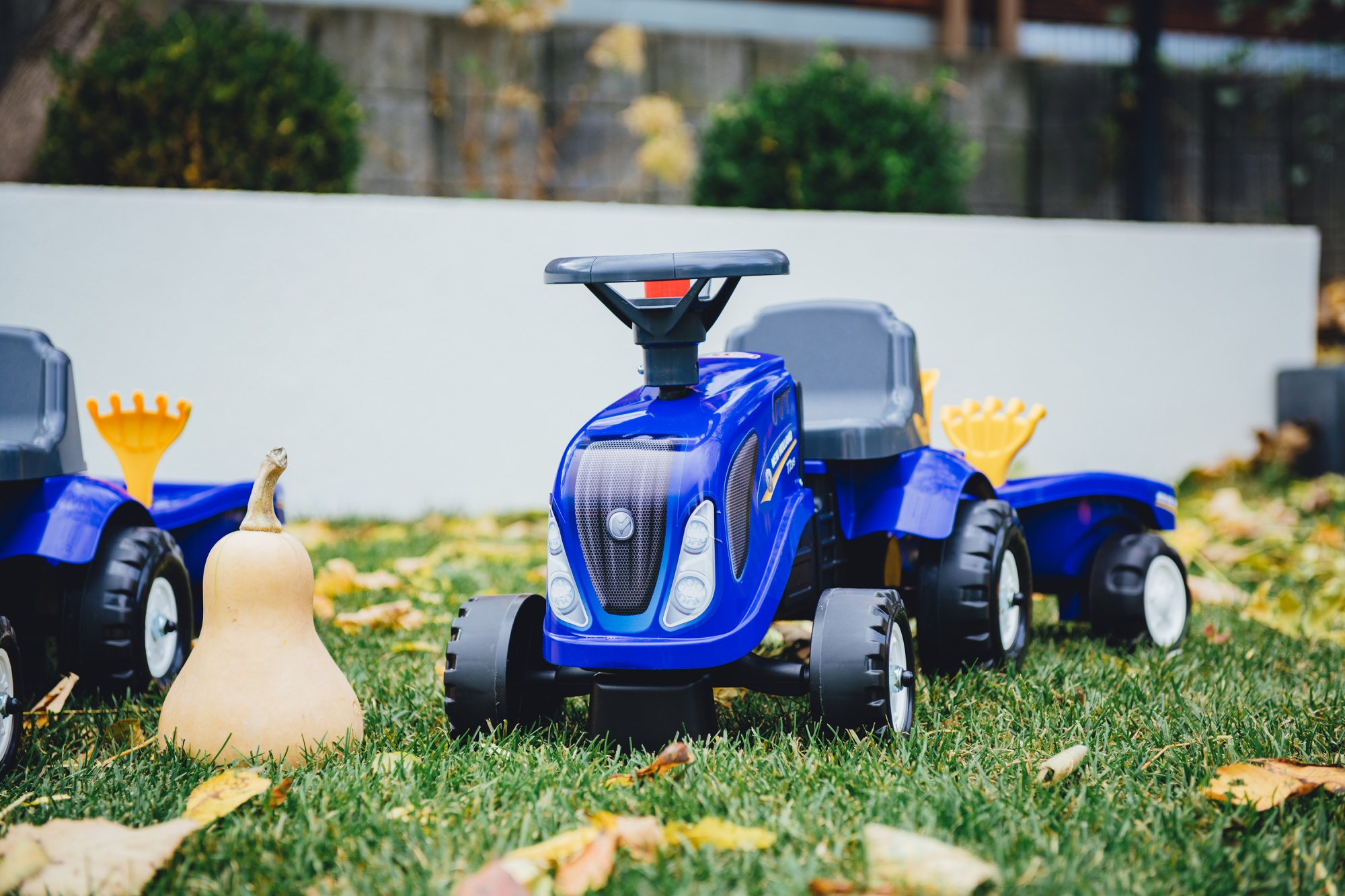 Un trattore giocattolo blu con una zucca davanti. Il trattore è sull'erba verde con un muro bianco sullo sfondo.