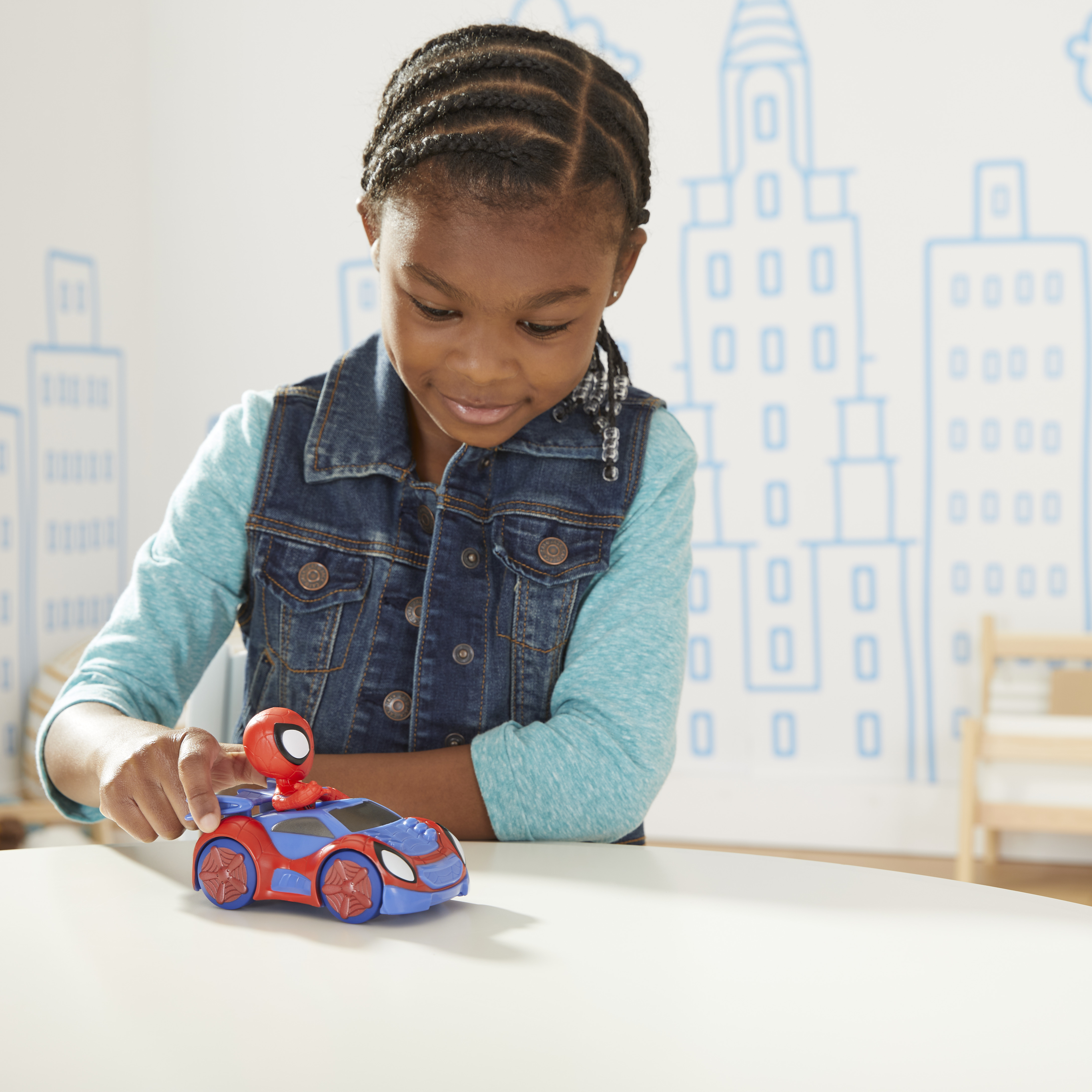 Dziewczynka bawi się zabawką Spider-Man na białym stole. Scena miejska jest na ścianie.