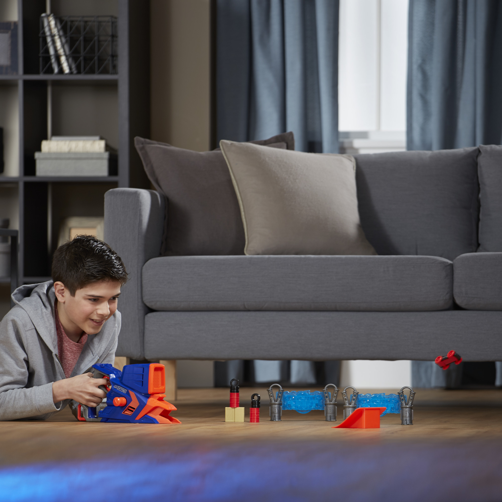 Chłopiec bawi się zestawem zabawek-samochodzików. Tor z przeszkodami jest ustawiony na podłodze.