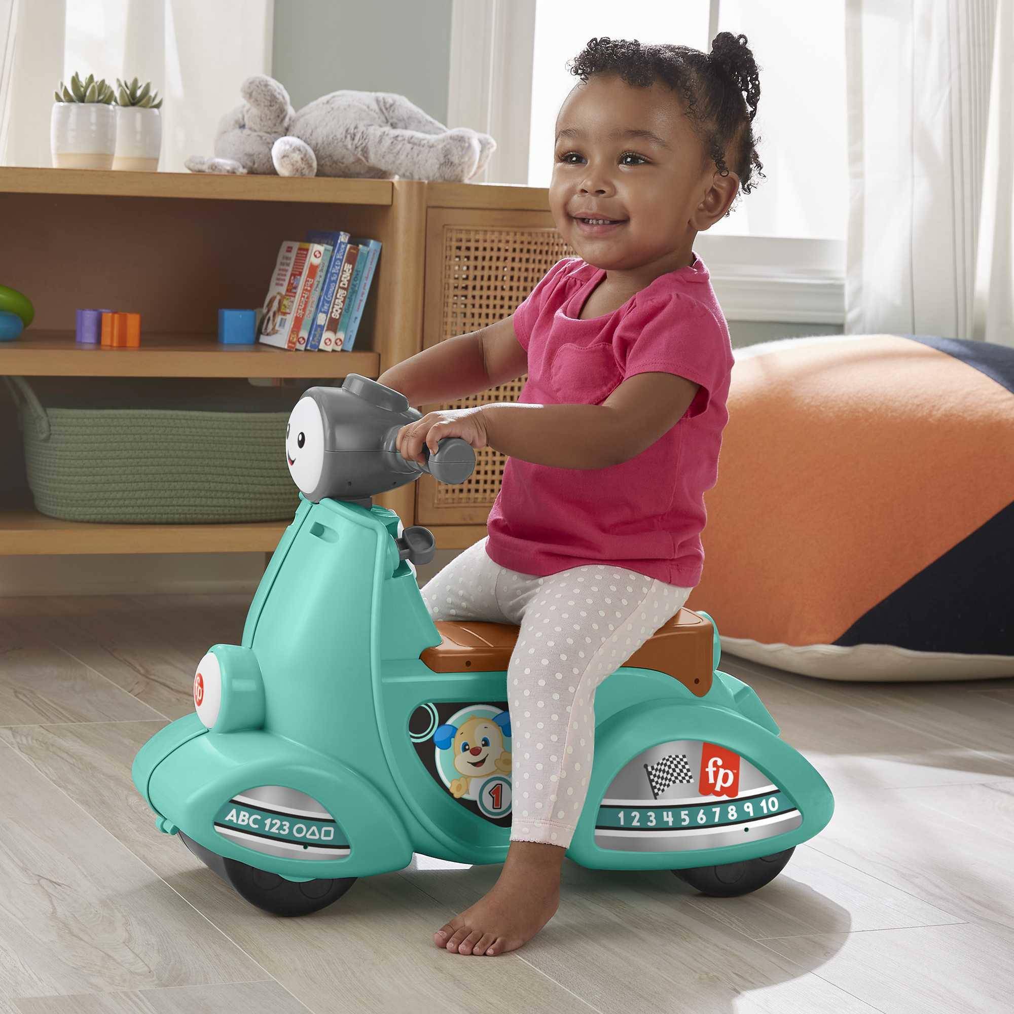 Bambino che guida un scooter giocattolo verde acqua. Sorridente, in casa.