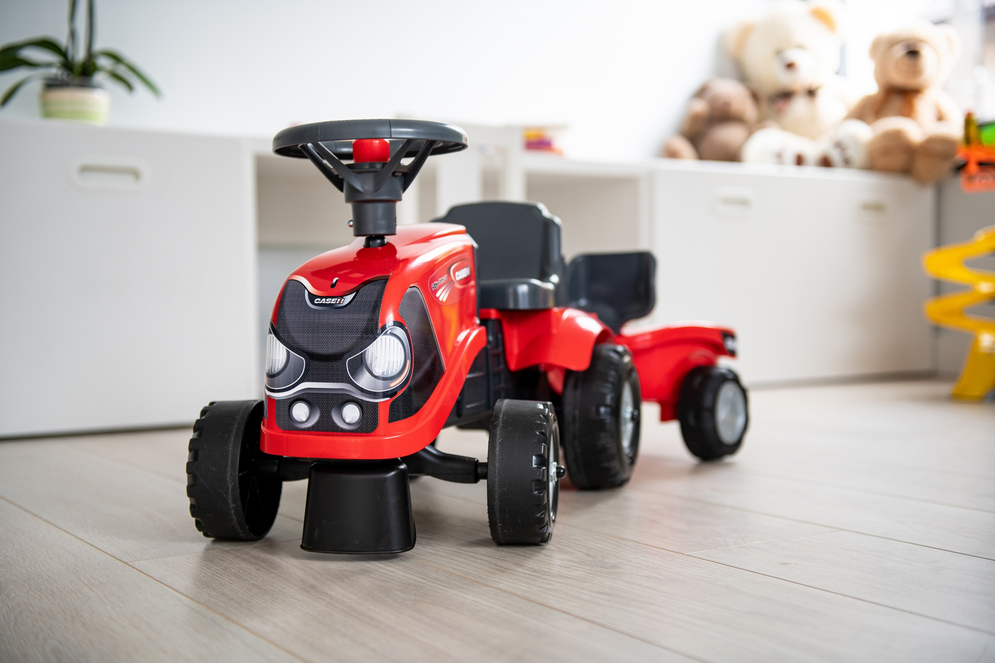 Juguete de tractor Case rojo sobre un piso de madera. Hay gabinetes blancos en el fondo.