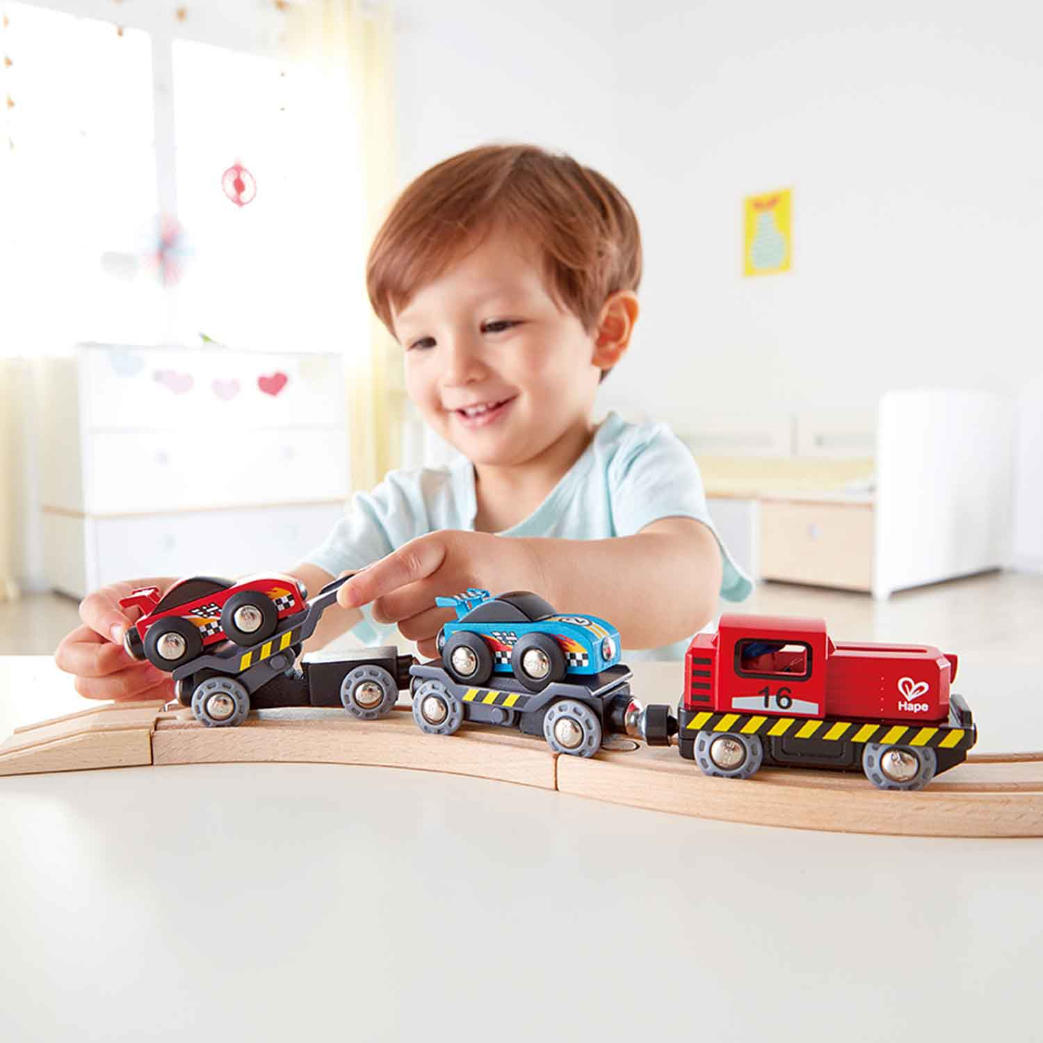 Un bambino che gioca con un set di treni giocattolo. Ci sono tre vagoni, uno rosso, uno blu e uno nero.