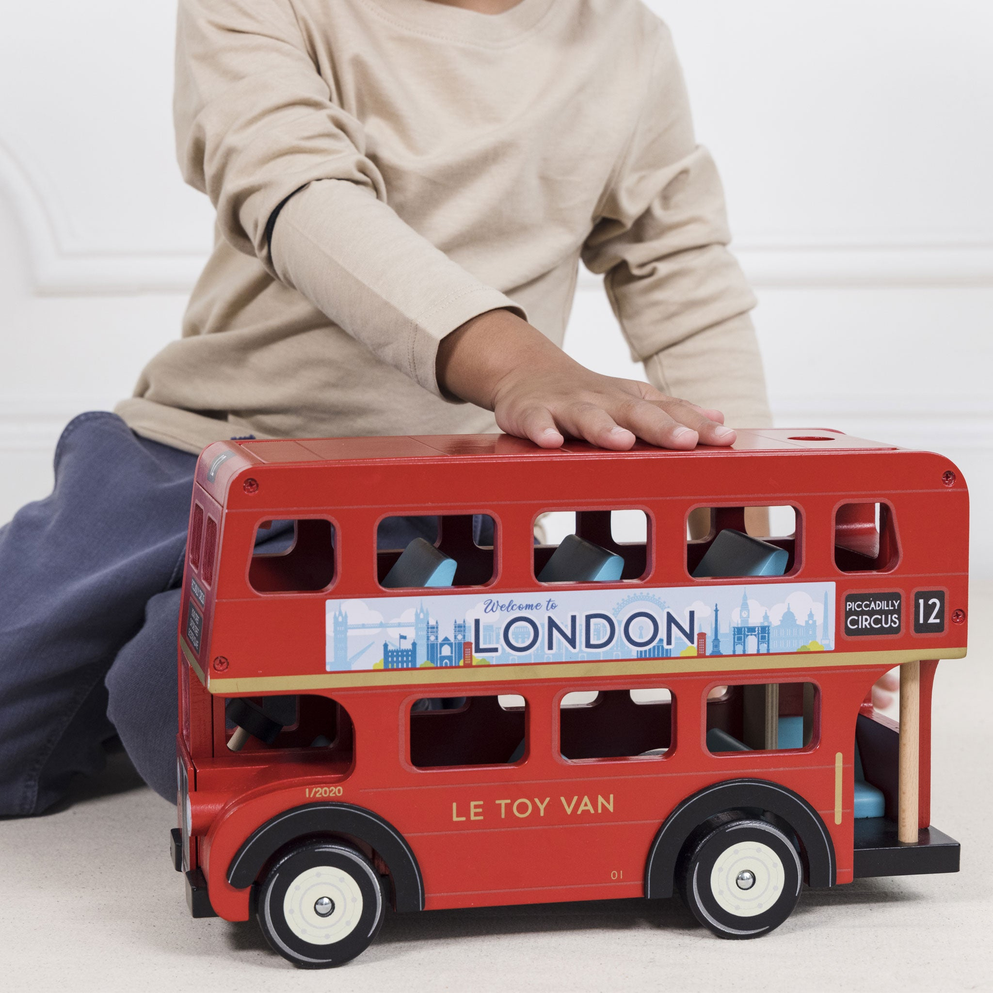 Ein Kind spielt mit einem roten Doppeldecker-London-Bus-Spielzeug. Der Bus trägt 'Welcome to London'.