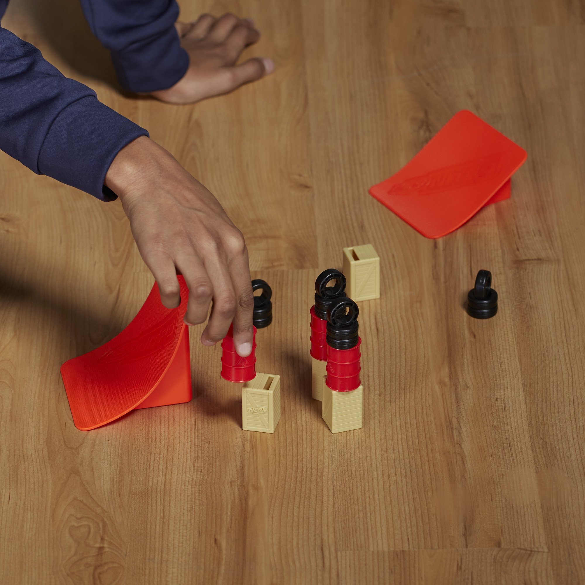 Ręce układają klocki i rampy na drewnianej powierzchni. Odcienie czerwieni i beżu.