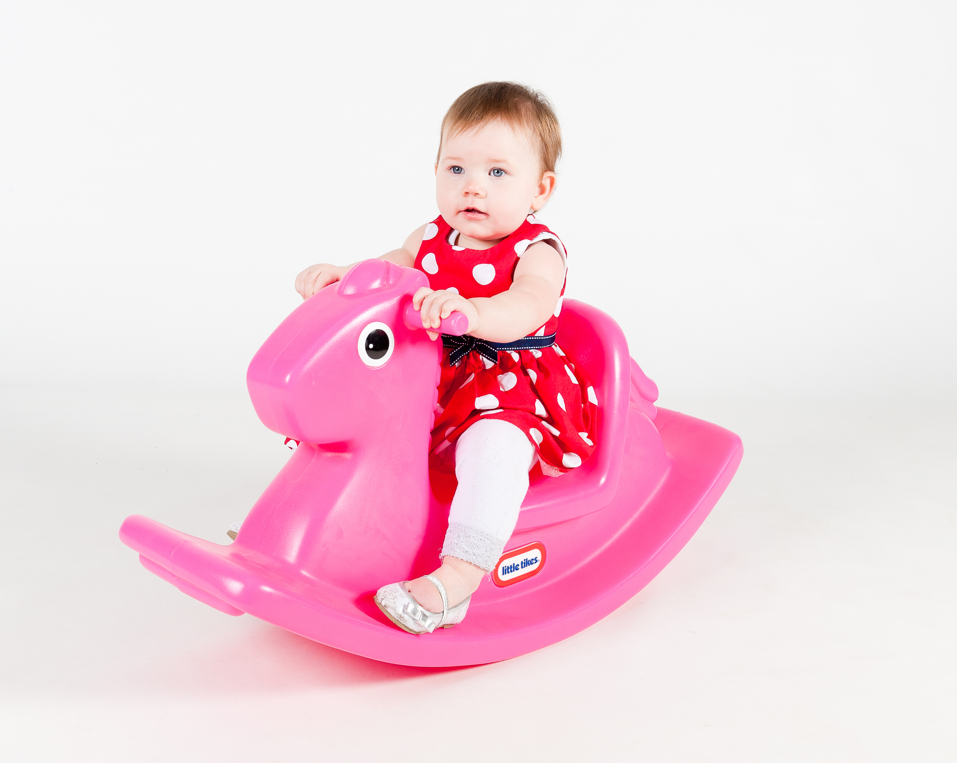 Una bambina in un vestito rosso su un cavallo a dondolo rosa, su sfondo bianco.