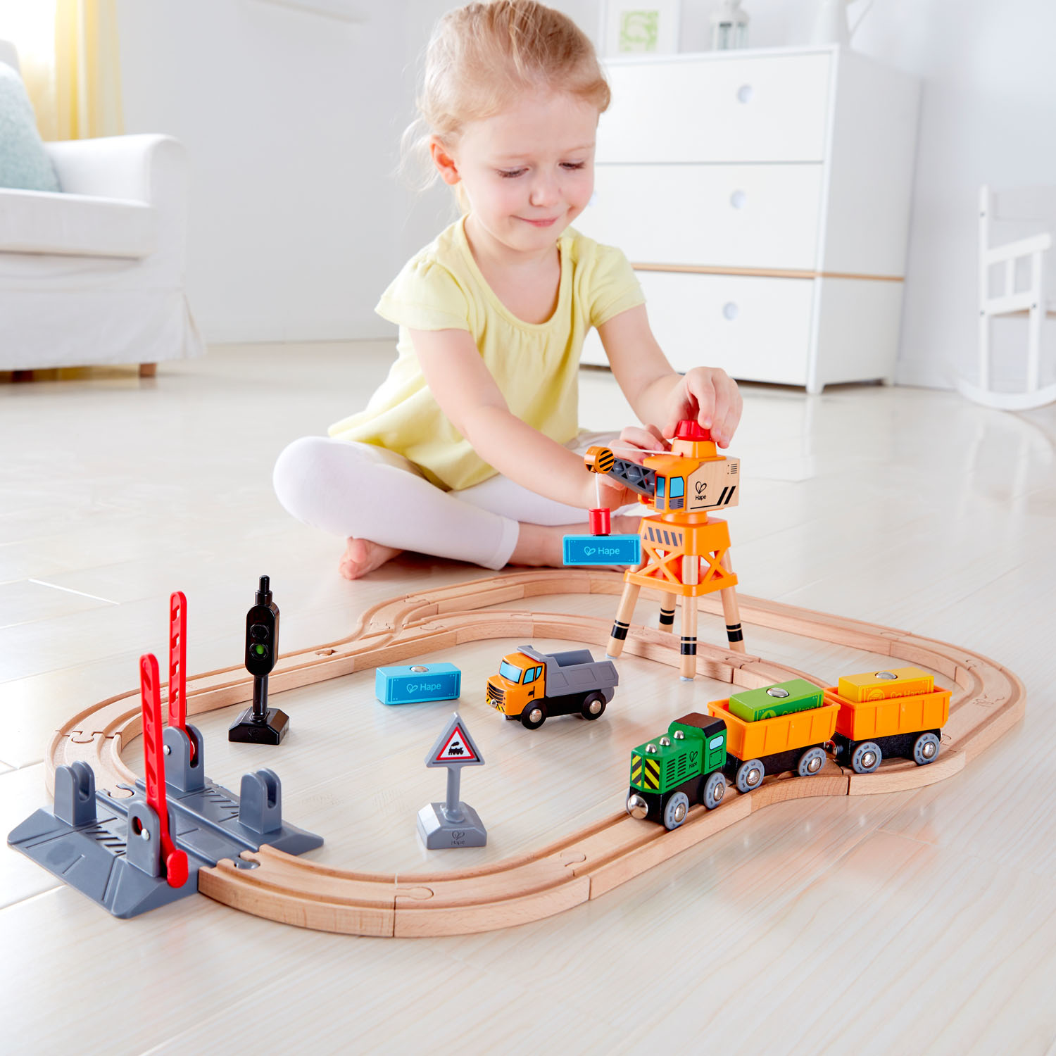 Una niña juega con un juego de trenes de madera, que incluye una grúa y vagones.