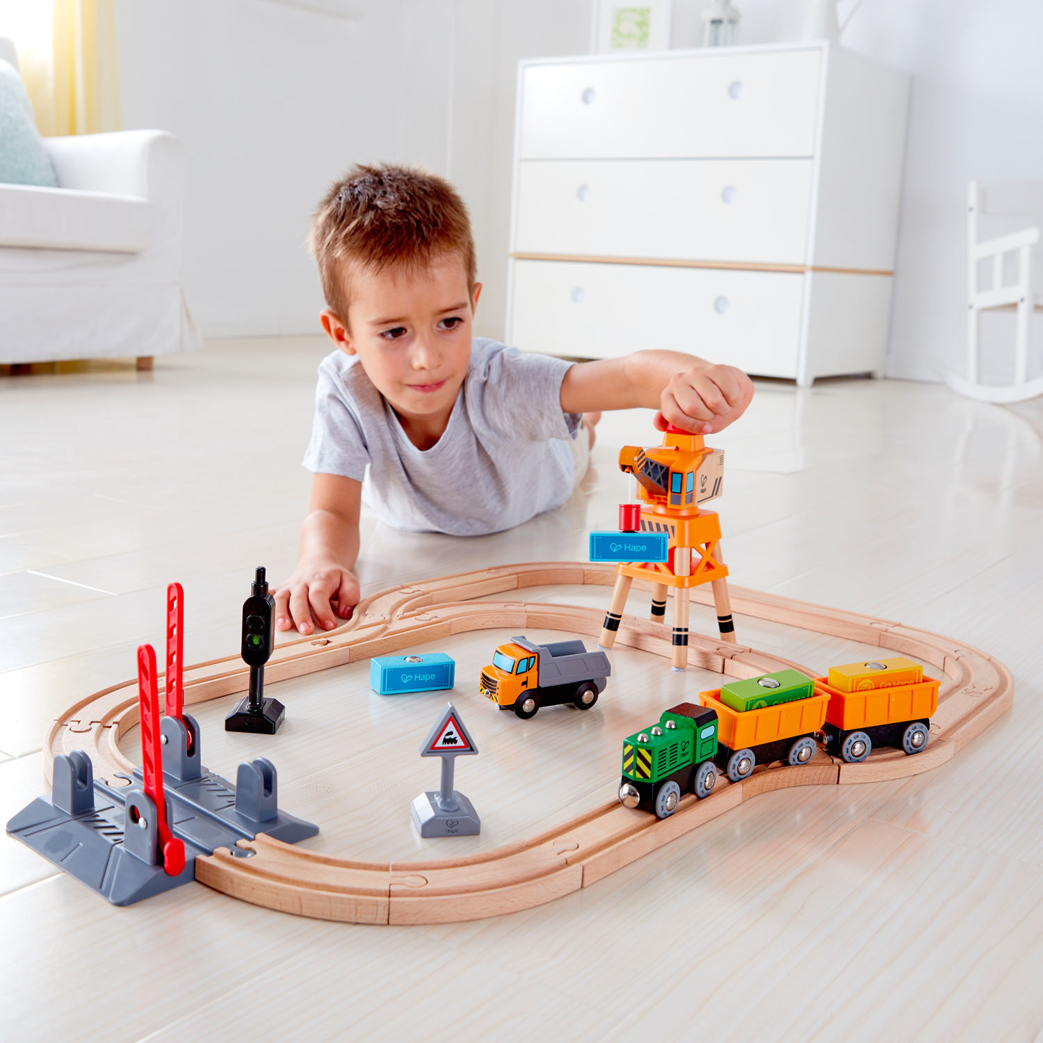 Un niño juega con un tren de juguete de madera, incluyendo trenes, una grúa y señales de tráfico.