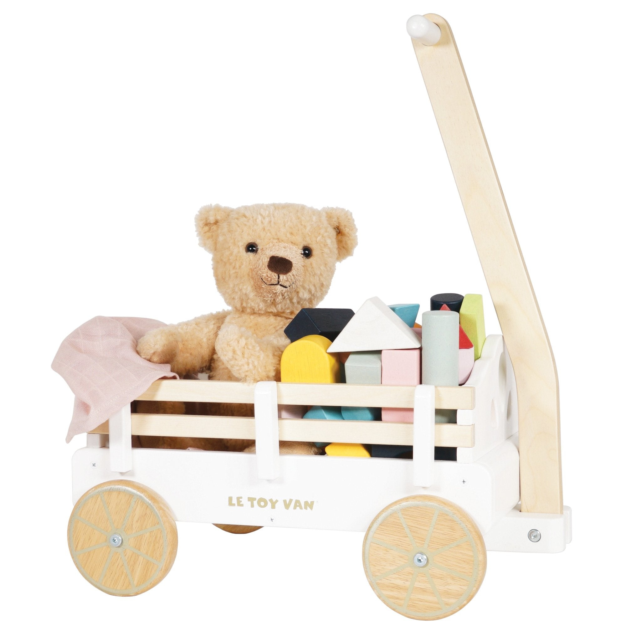 Ein Holzspielzeugwagen mit bunten Blöcken, einem Teddybär und einer rosa Decke gefüllt.