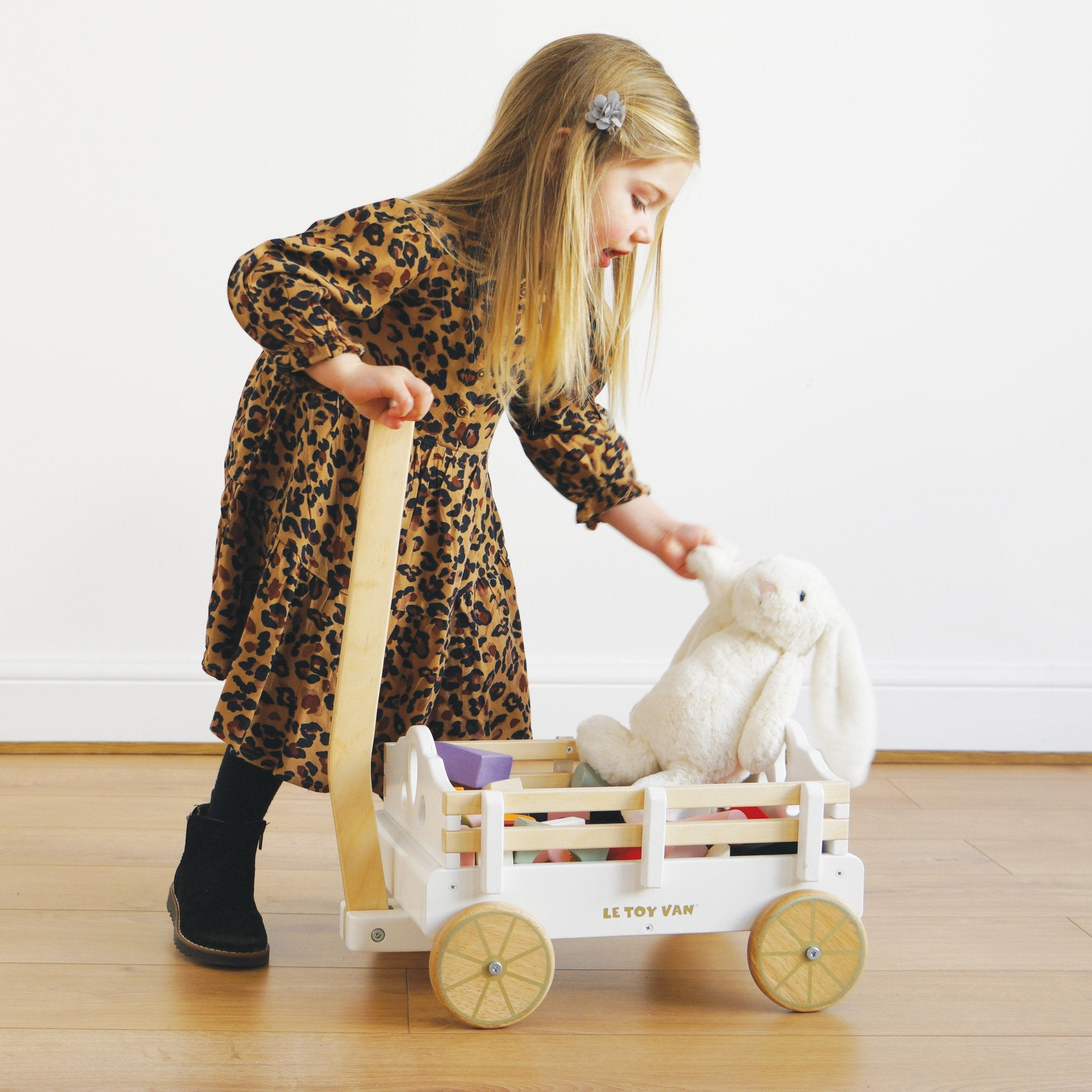 Ein Mädchen spielt mit einem Holzspielzeugwagen und legt einen weißen Stoffhasen hinein.