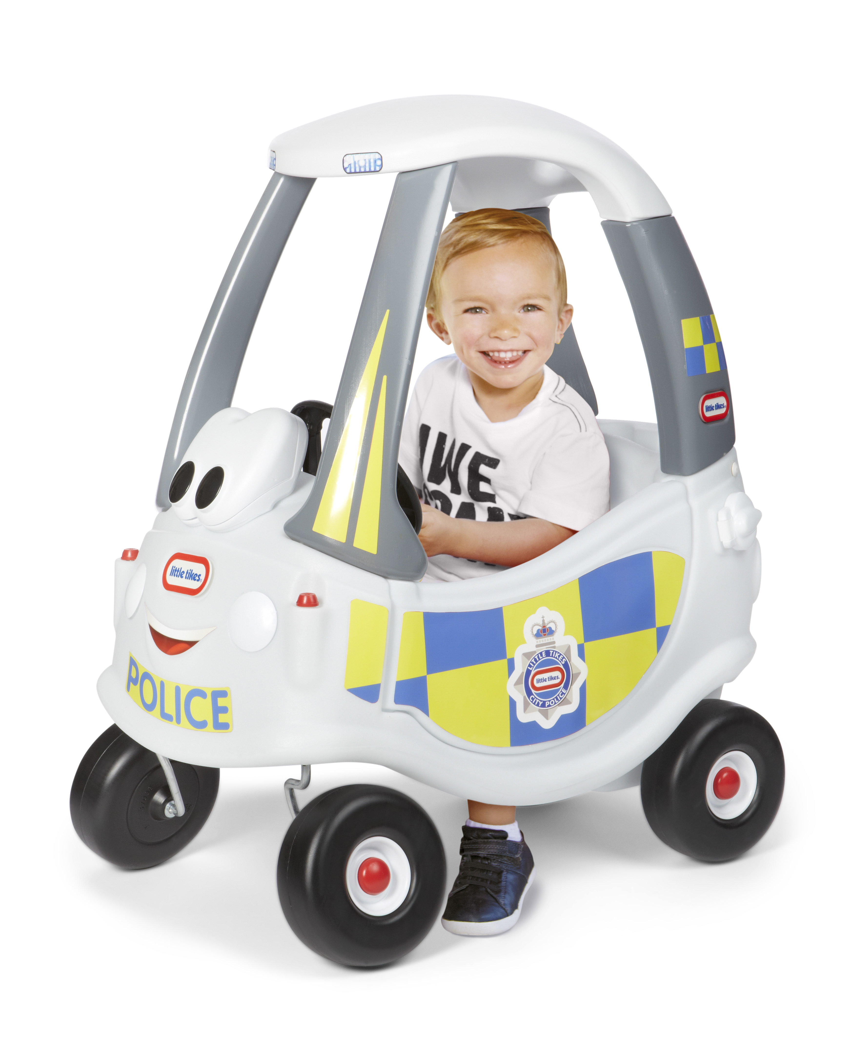 Un bambino sorridente in un'auto della polizia giocattolo bianca. L'auto è bianca, con tetto grigio e pneumatici neri.
