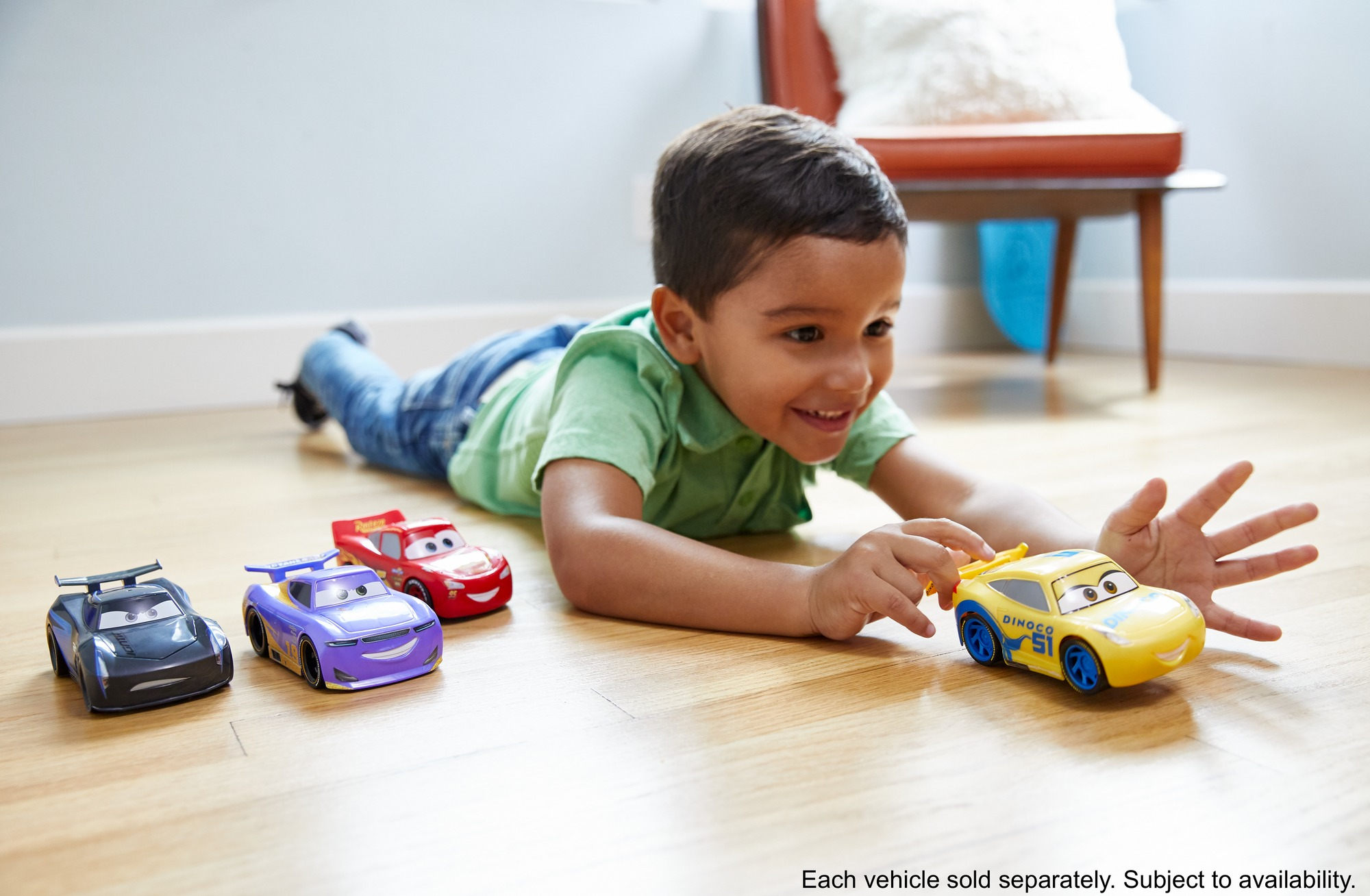 Dziecko bawi się samochodzikami na drewnianej podłodze. Samochody są czerwone, fioletowe, czarne i żółte.