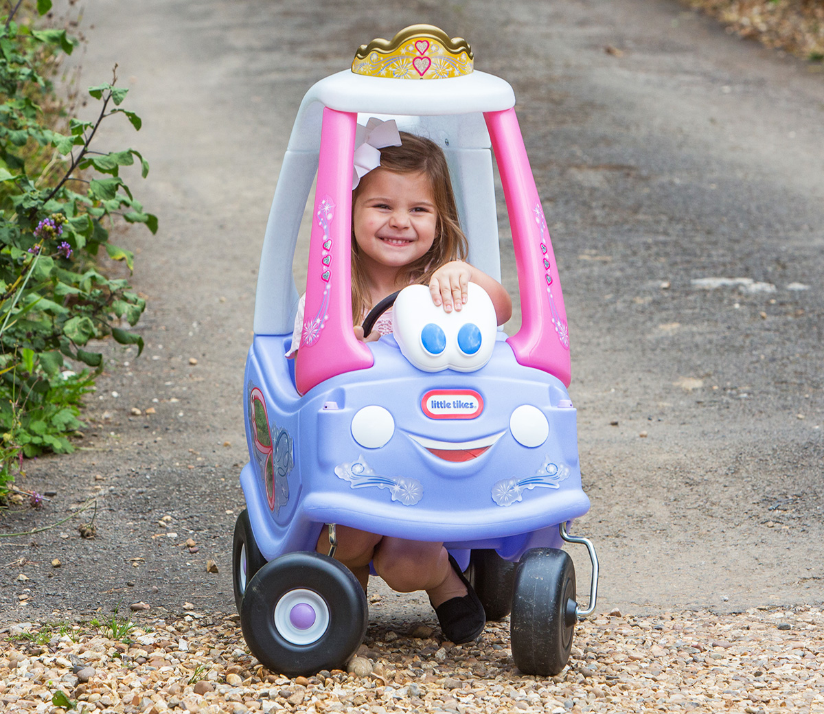Una ragazzina è seduta in un'auto giocattolo rosa e viola. Sta sorridendo.