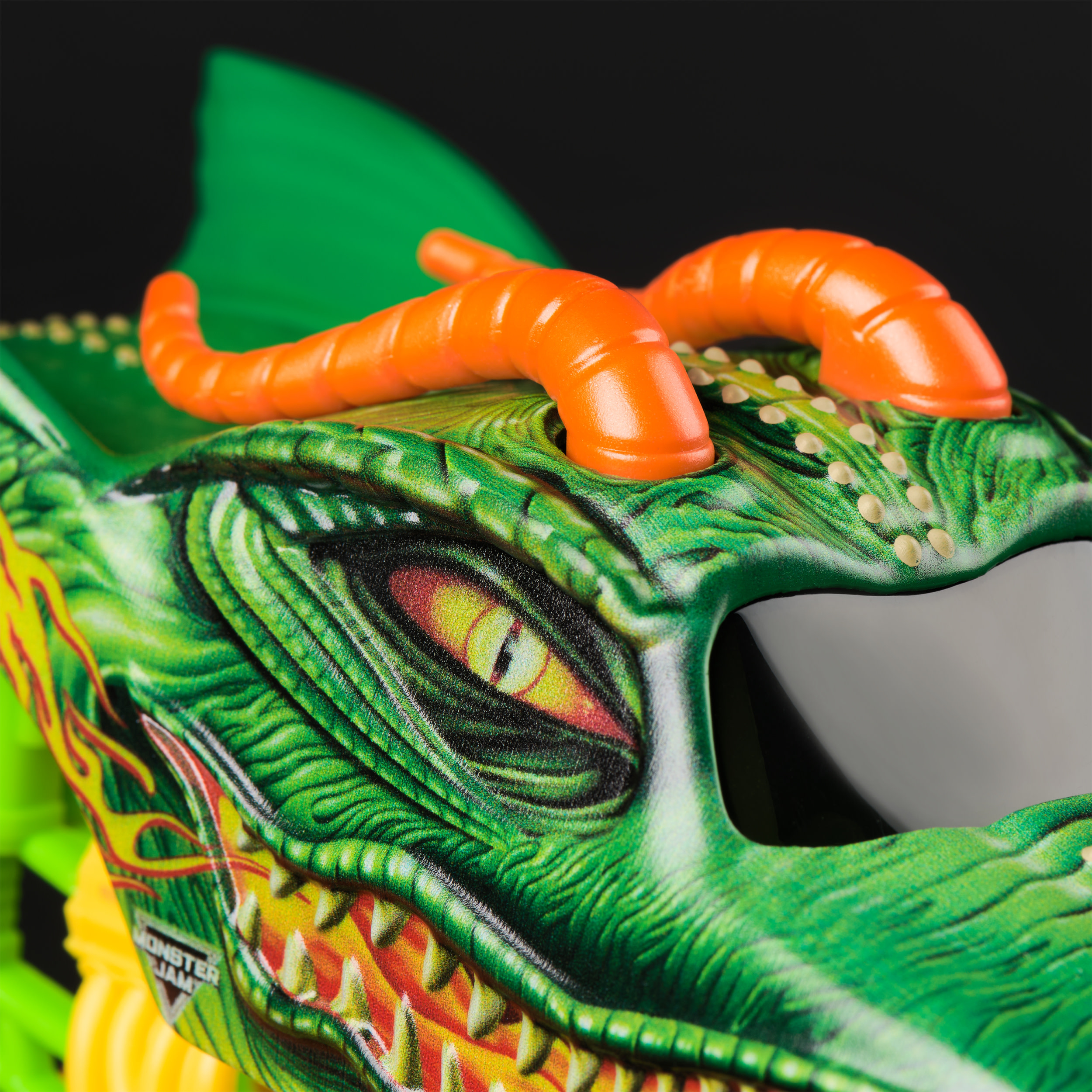 Zielona ciężarówka potworów z motywem smoczej twarzy, pomarańczowymi rogami i kołami.