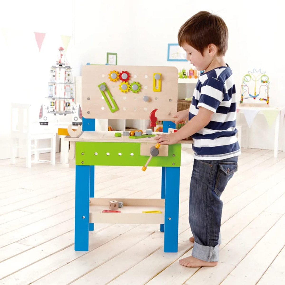 Dziecko bawiące się drewnianym warsztatem. Warsztat jest zielono-niebieski. Tło to pokój.