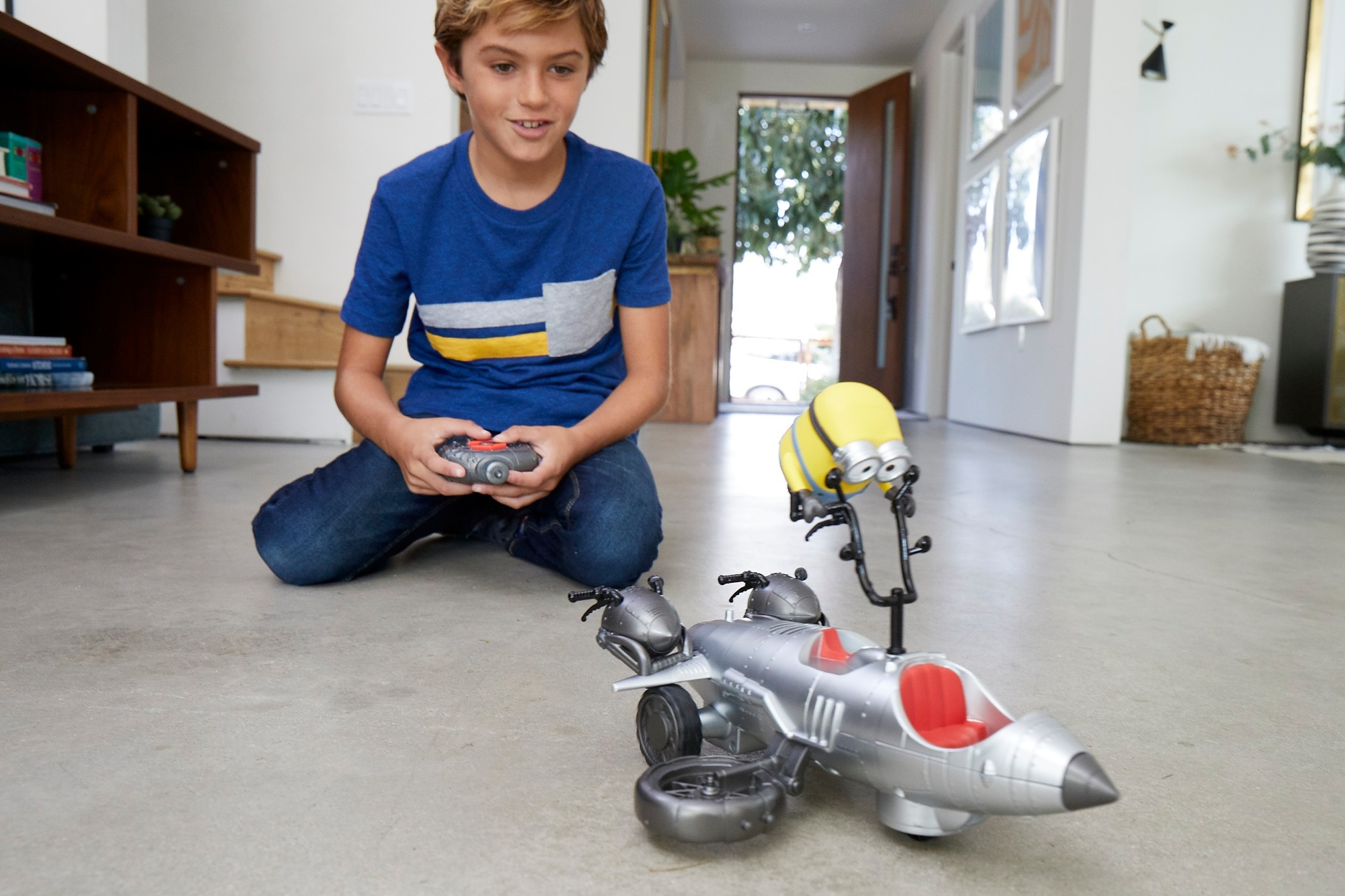 Chłopiec bawi się zabawkowym pojazdem Minionków. Pojazd jest srebrny z figurką Minionka na górze.