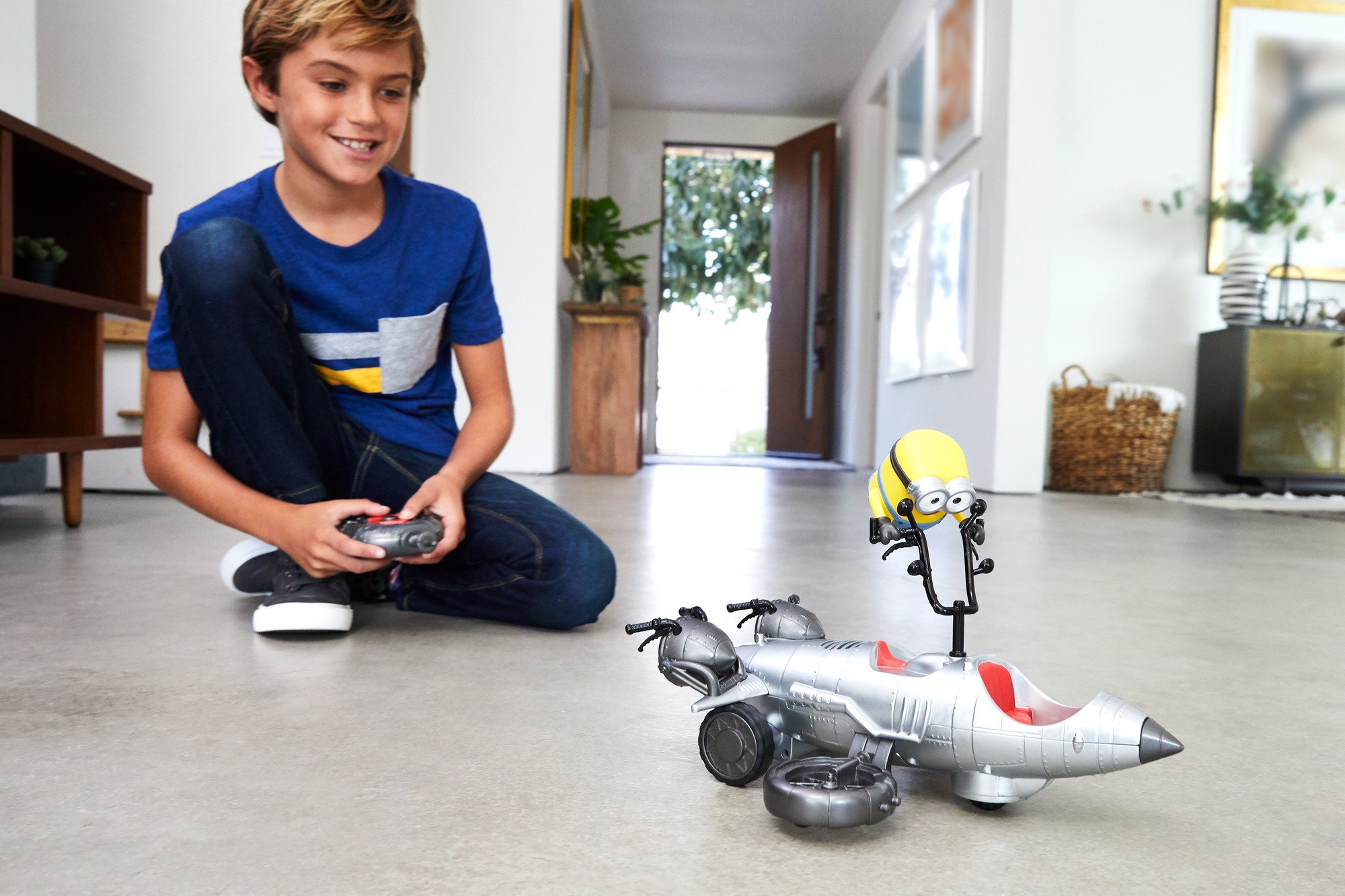 Chłopiec bawi się zabawką-odrzutowcem z figurką Minionka. Uśmiecha się i trzyma pilota.