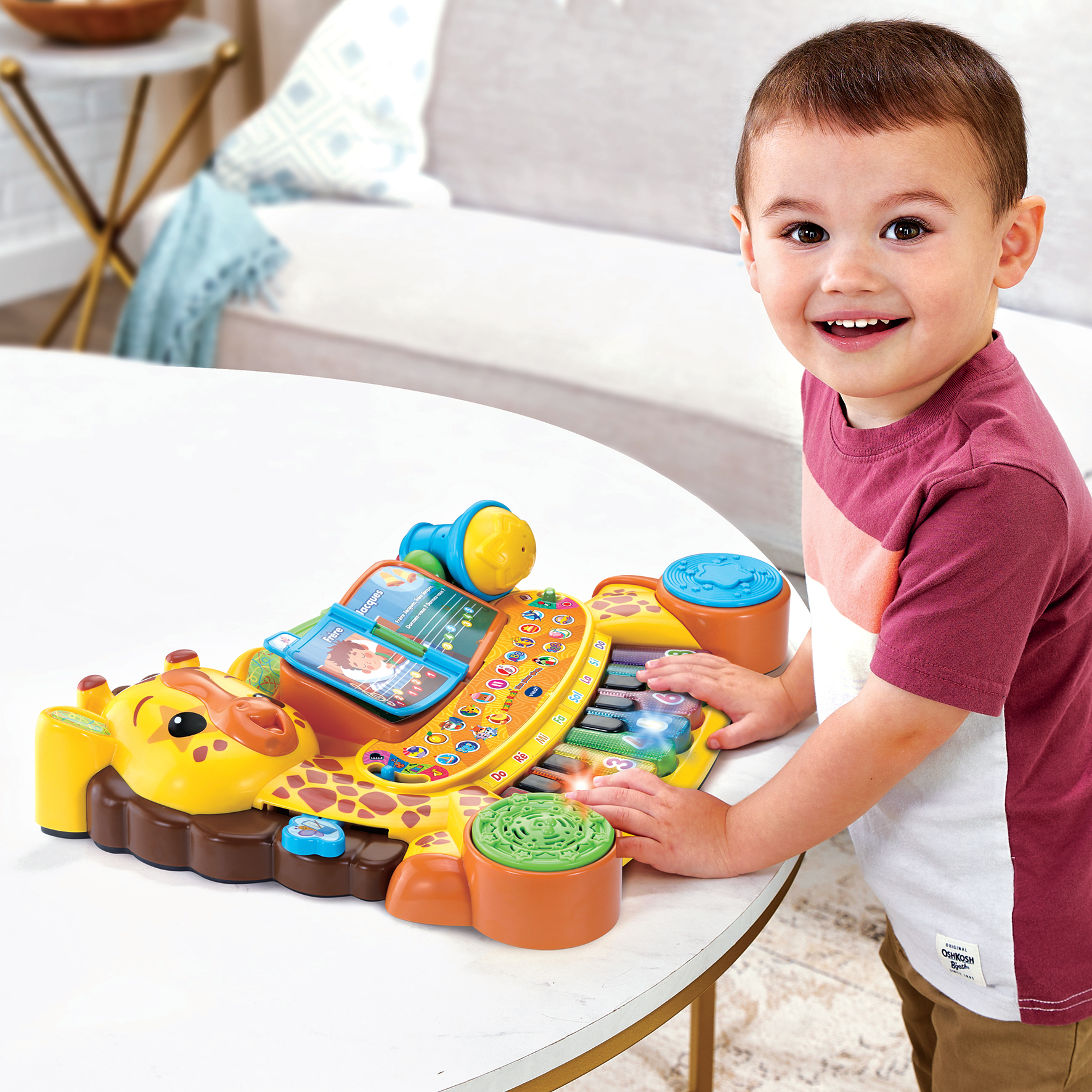 Un niño sonriente está de pie junto a un piano de juguete de jirafa amarilla.