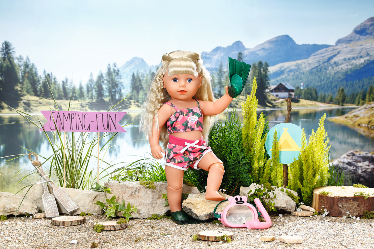 Una muñeca en traje de baño sosteniendo una aleta. El lago y las montañas están en el fondo.