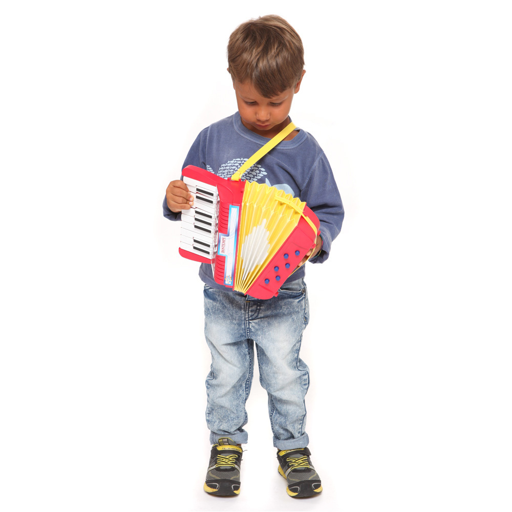 Ein Junge spielt stehend ein rotes und gelbes Spielzeugakkordeon. Blaues Hemd, Jeans. Weißer Hintergrund.
