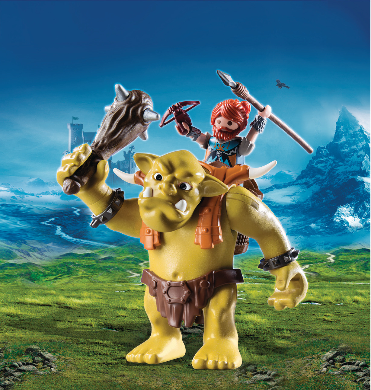 Zabawka przedstawia zielonego trolla z wojownikiem na grzbiecie. W tle zamek i błękitne niebo.