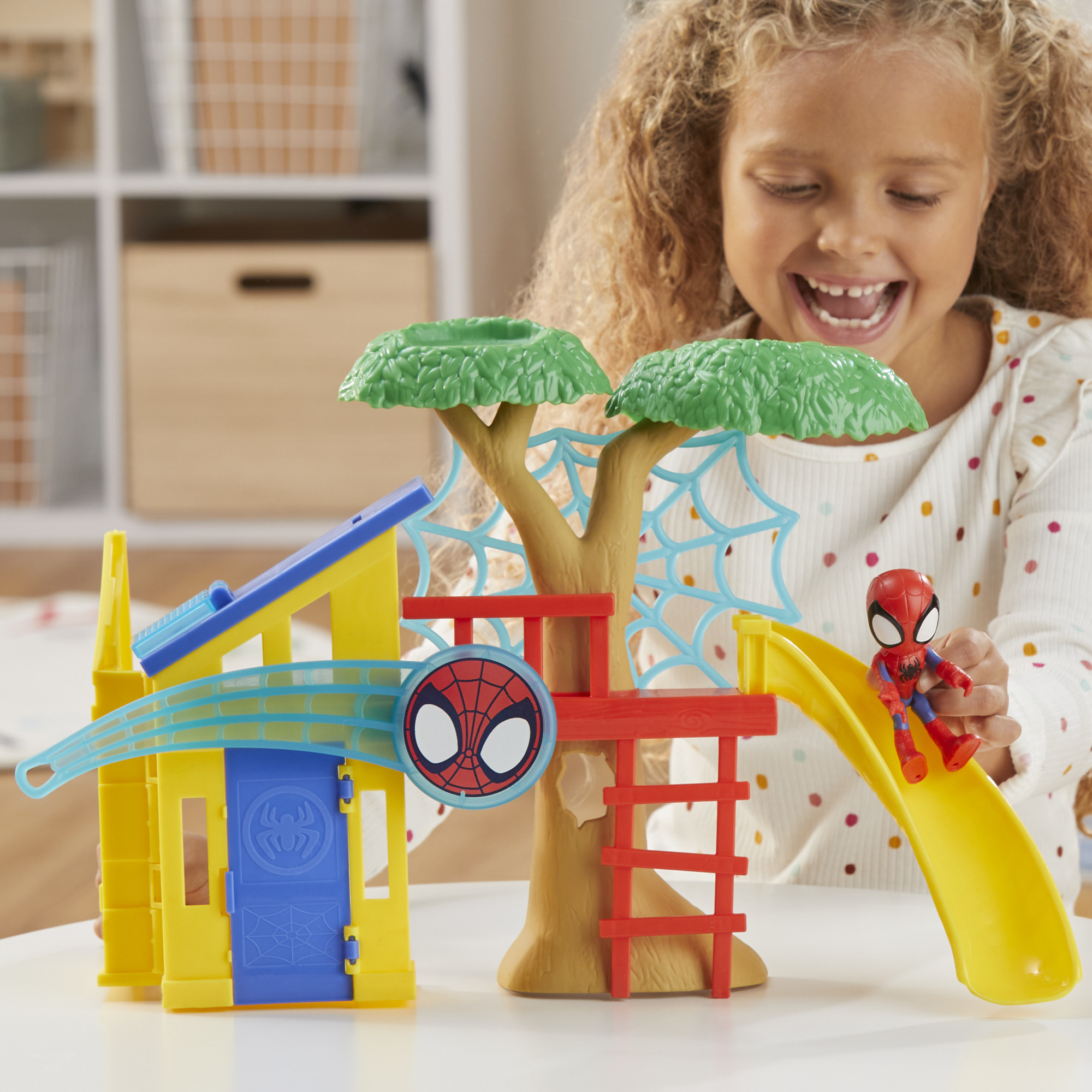Una bambina sorride mentre gioca con un set di giocattoli di Spider-Man, con una casa sull'albero, uno scivolo e una figura.