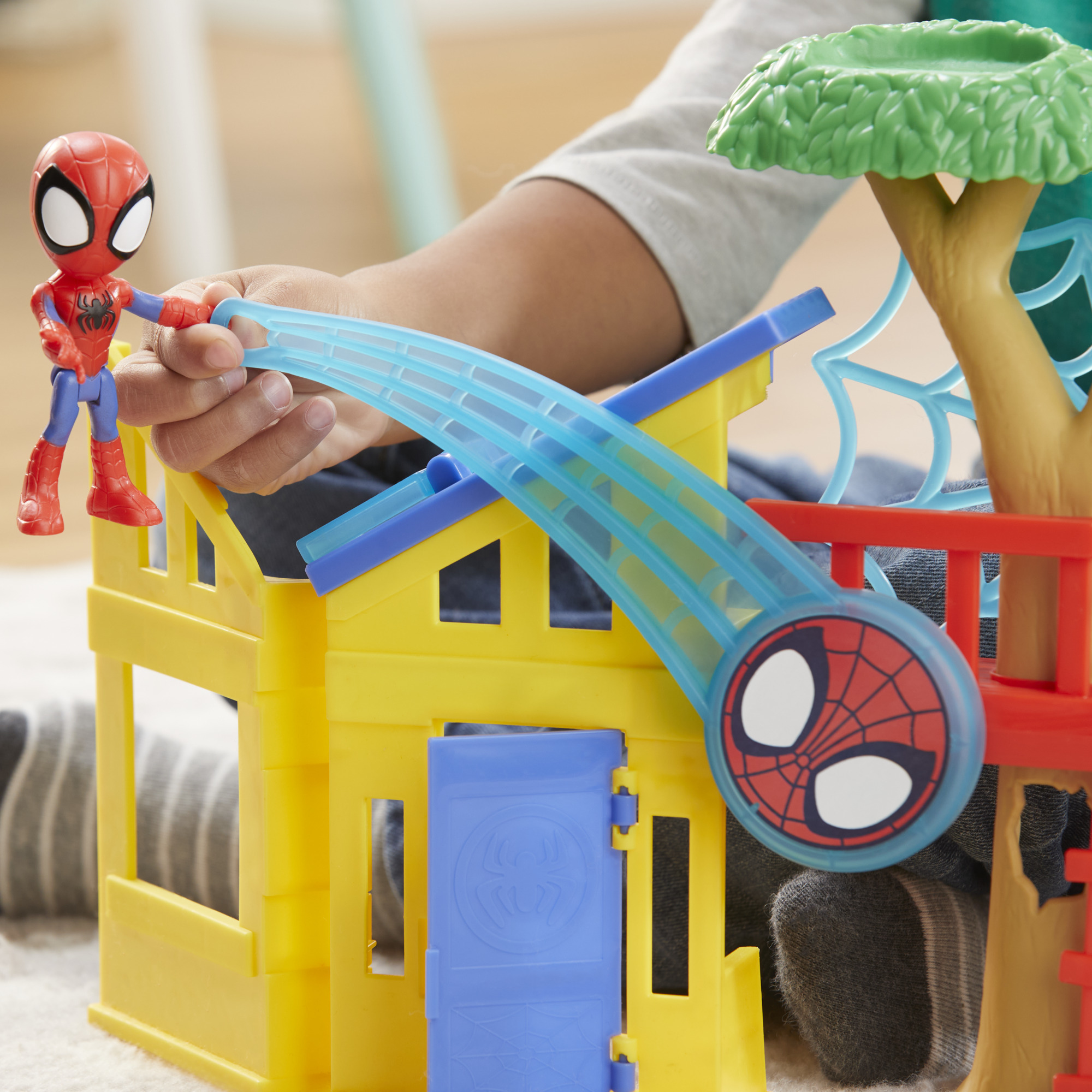 La mano di un bambino che interagisce con un set di giocattoli di Spider-Man con una casa sull'albero, uno scivolo e un personaggio.