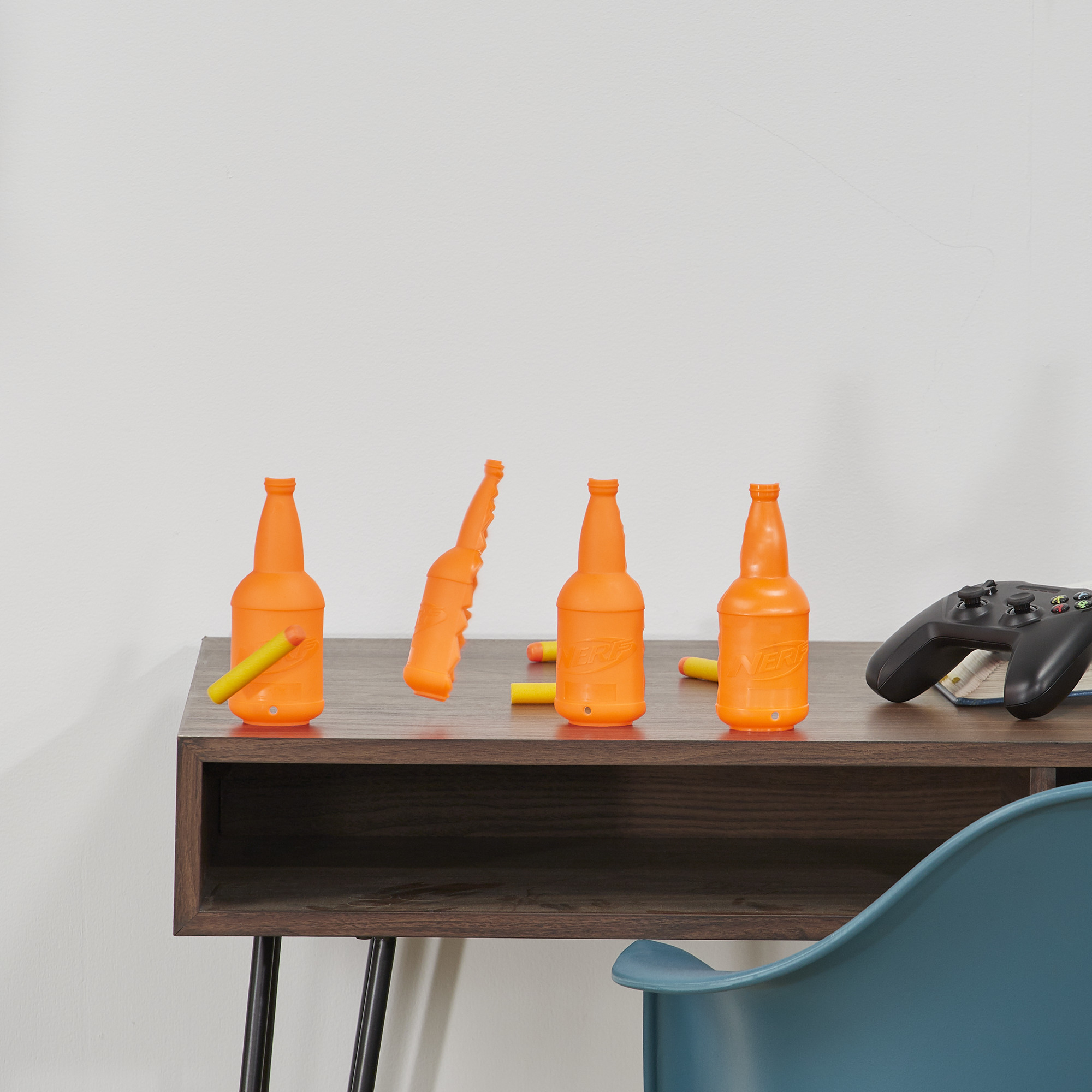 Botellas y dardos naranjas en mesa de madera, con mando de videojuegos.