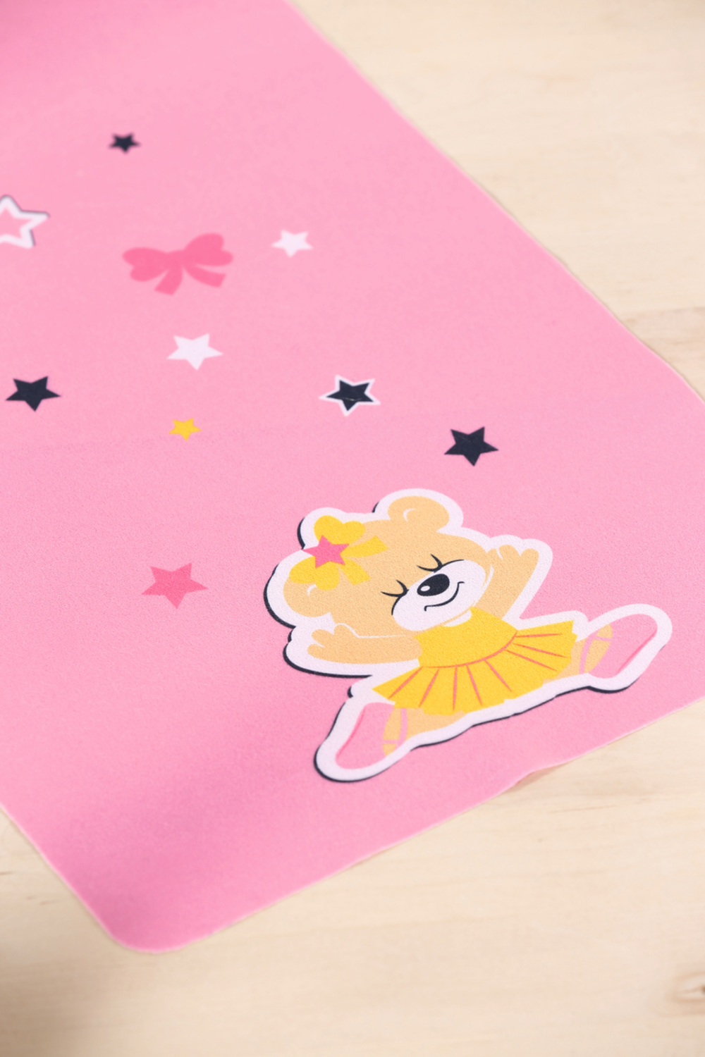 Różowa karta z naklejką tańczącego misia i gwiazdami. Drewniany stół w tle.