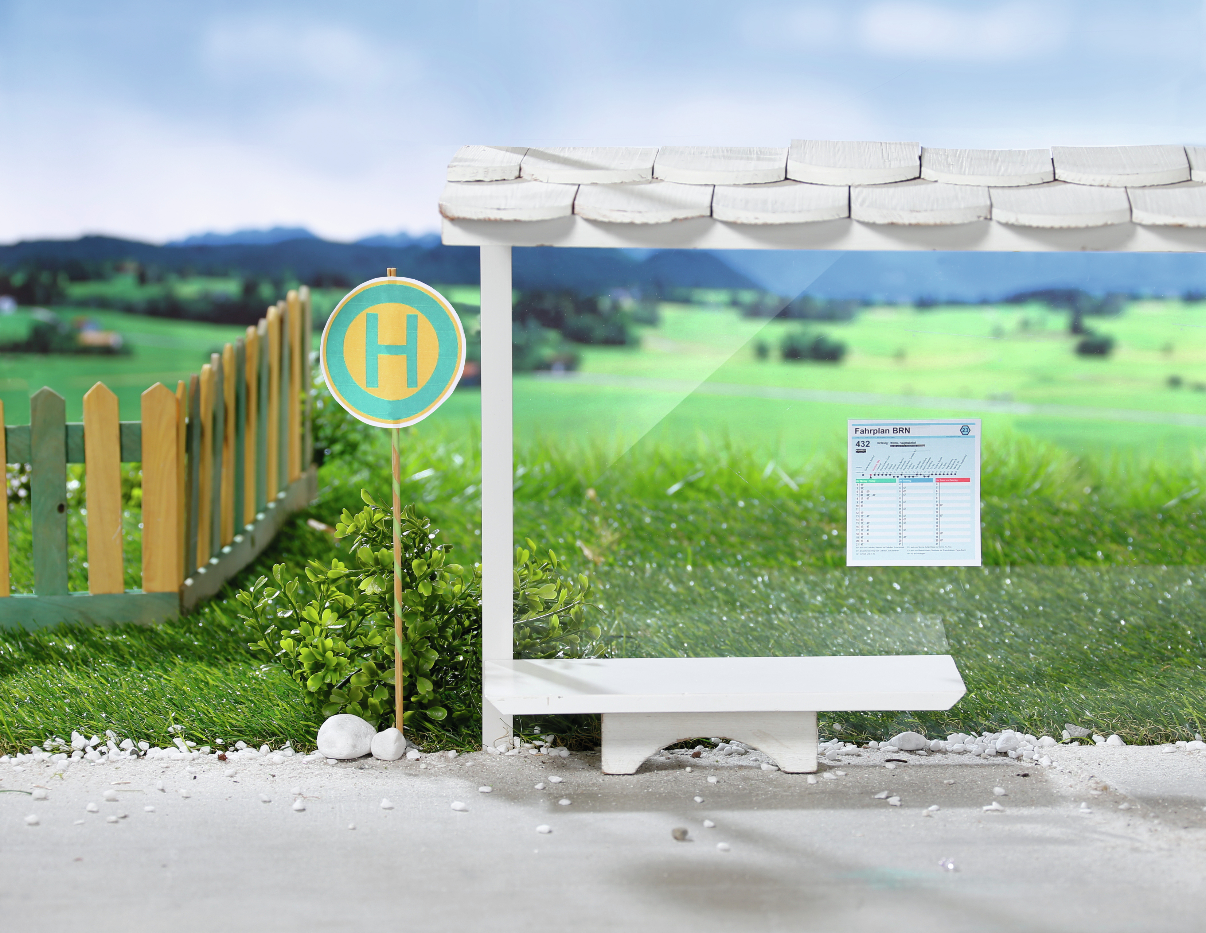 Scena przystanku autobusowego z zabawkami. Przystanek z tablicą i ławką. Zielone tło z trawą.