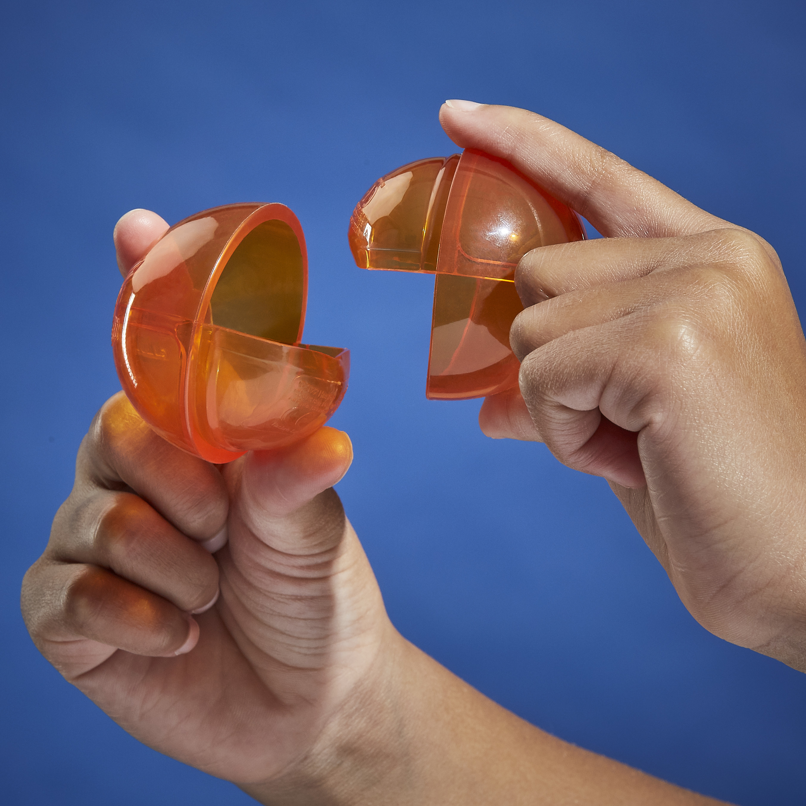 Dwie dłonie rozdzielające pomarańczową, przezroczystą plastikową kulę na niebieskim tle.