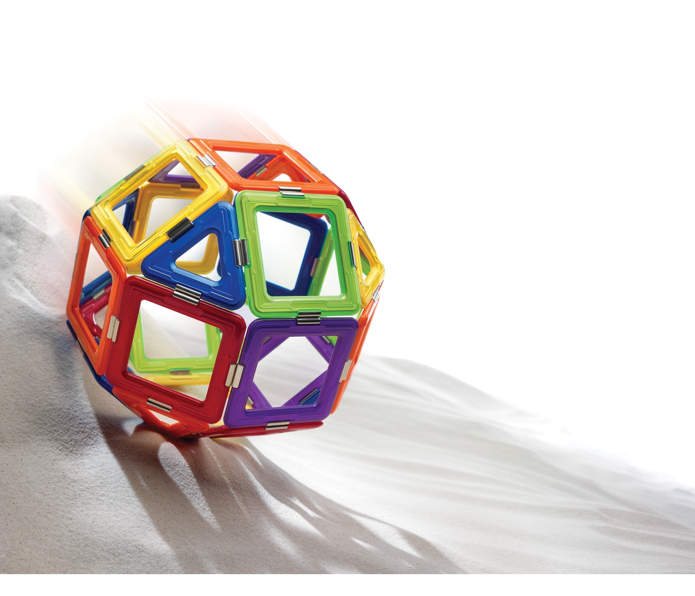 Una palla geometrica colorata rotola sulla sabbia. La palla è fatta di quadrati colorati collegati.