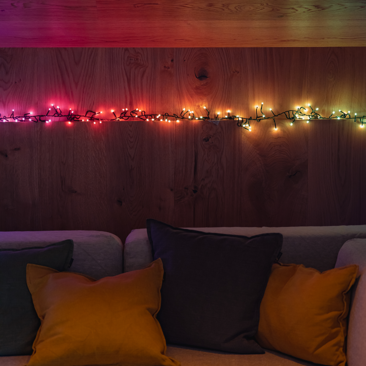 Sofa z poduszkami na tle drewnianej ściany. Szereg kolorowych świateł jest przymocowany do ściany powyżej.