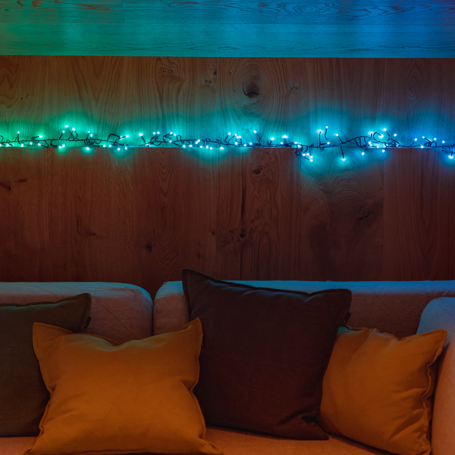 Sofa z poduszkami na tle drewnianej ściany. Szereg kolorowych świateł jest przymocowany do ściany powyżej.
