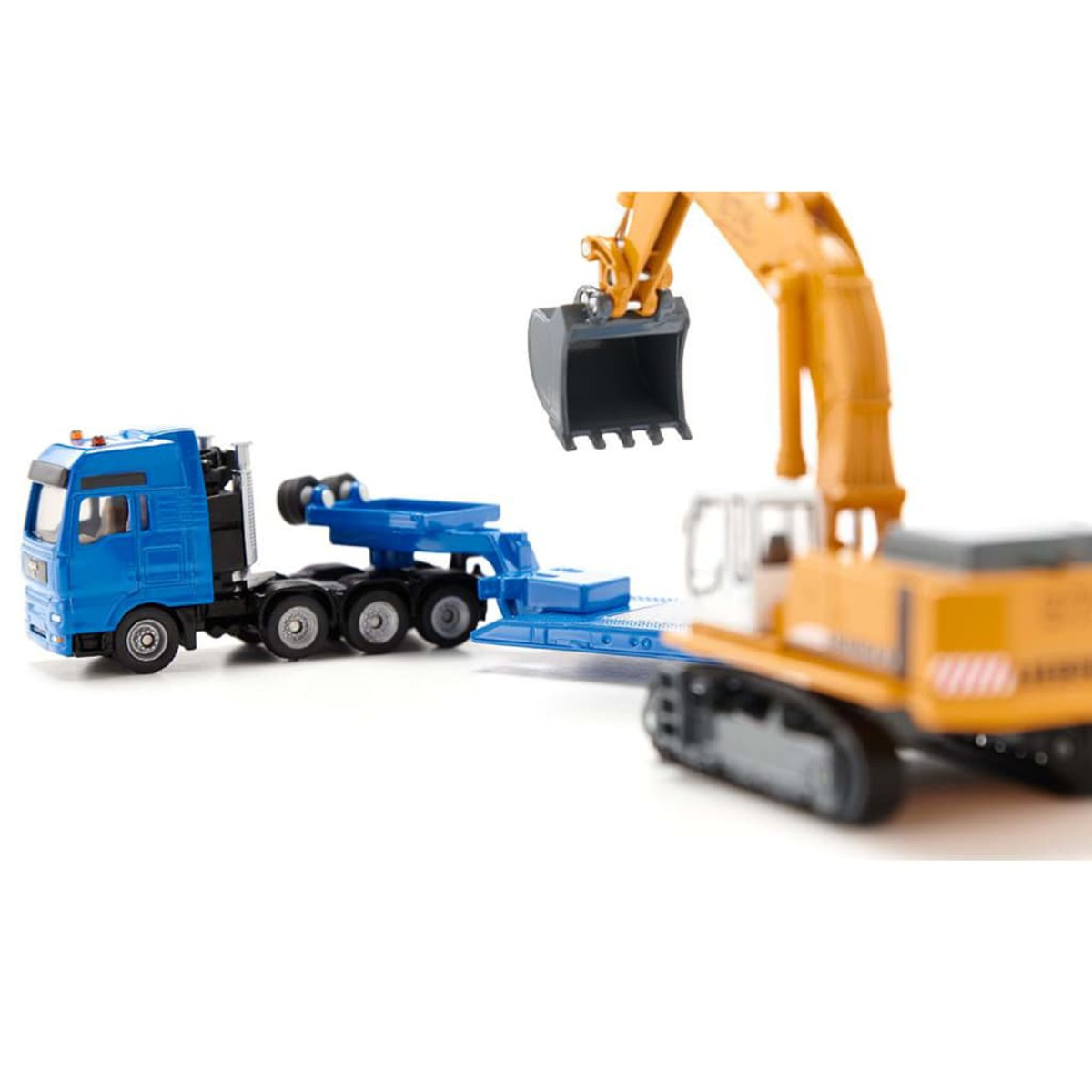 Spielzeugbagger und Anhänger, die von einem blauen LKW gezogen werden. Der Bagger ist gelb und weiß.