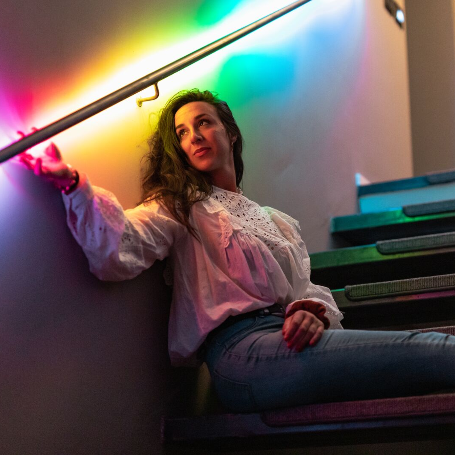 Une femme avec des lumières colorées sur un escalier, appuyée contre une rampe. Les lumières sont allumées.