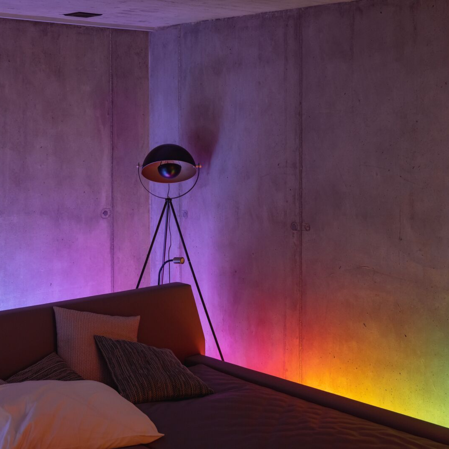 Chambre avec un lit et une lampe. Les murs sont en béton et la pièce est éclairée par des lumières colorées.