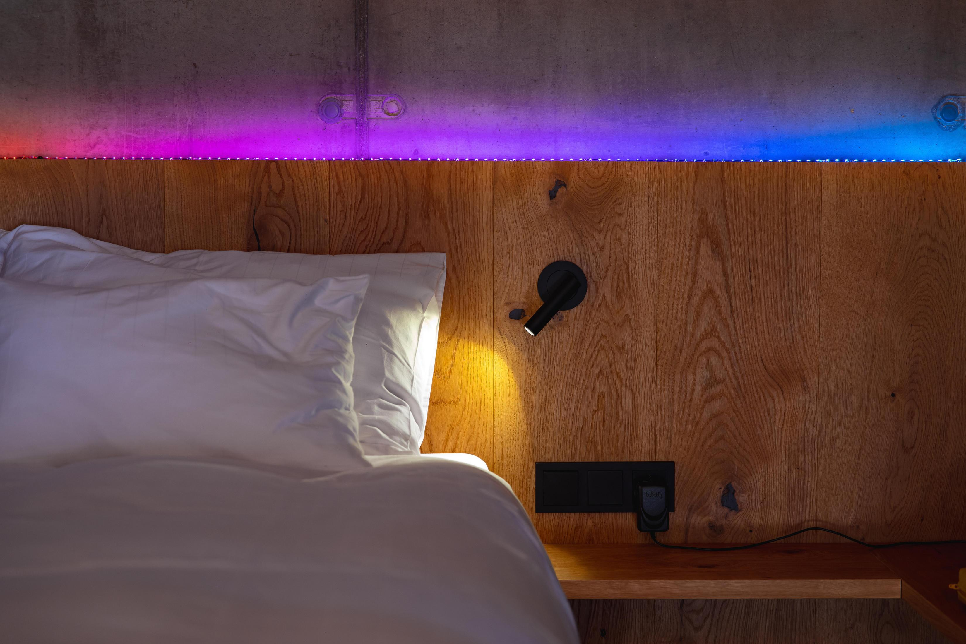 Un lit avec des oreillers contre un mur en bois. Une lumière brille et des lumières colorées au-dessus.