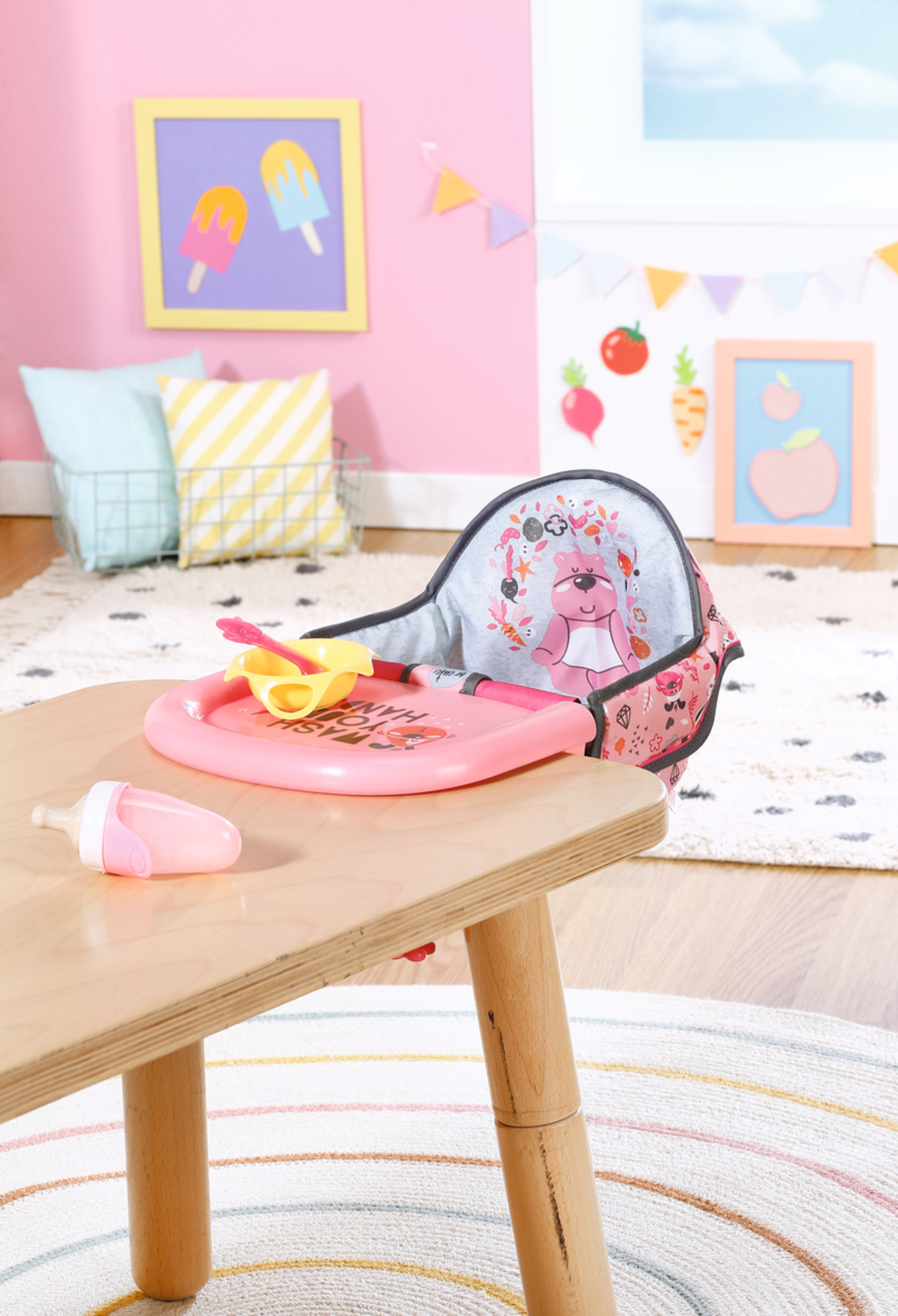 Krzesełko do karmienia dla lalek, różowy stół i butelka na drewnianym stole.
