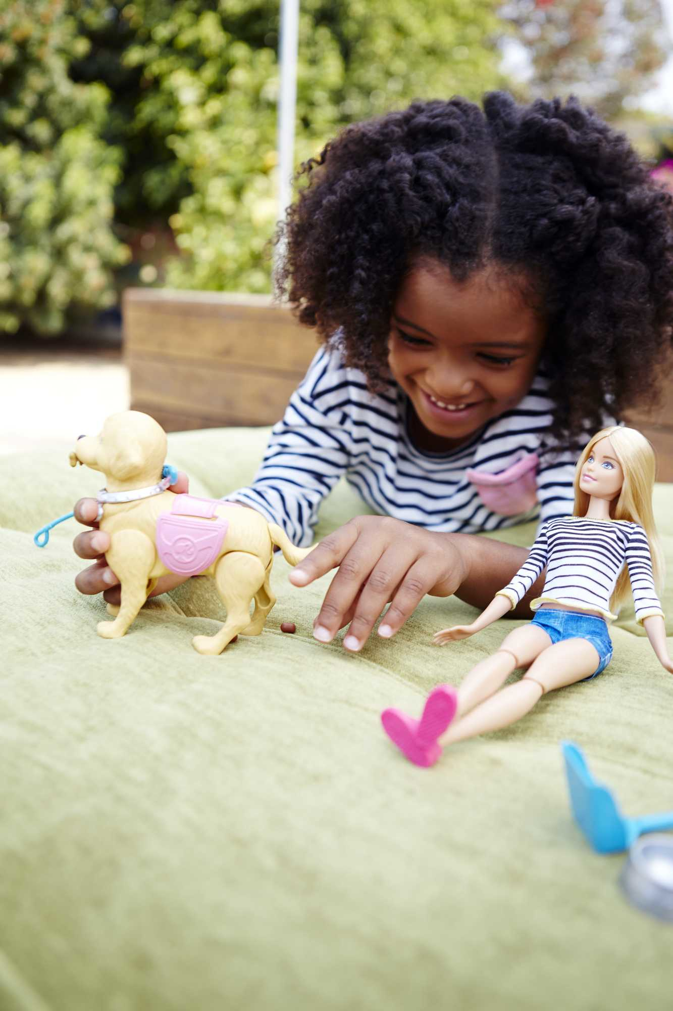 Dziewczynka i lalka Barbie bawią się zabawką w psa. Pies ma różowe siodło.