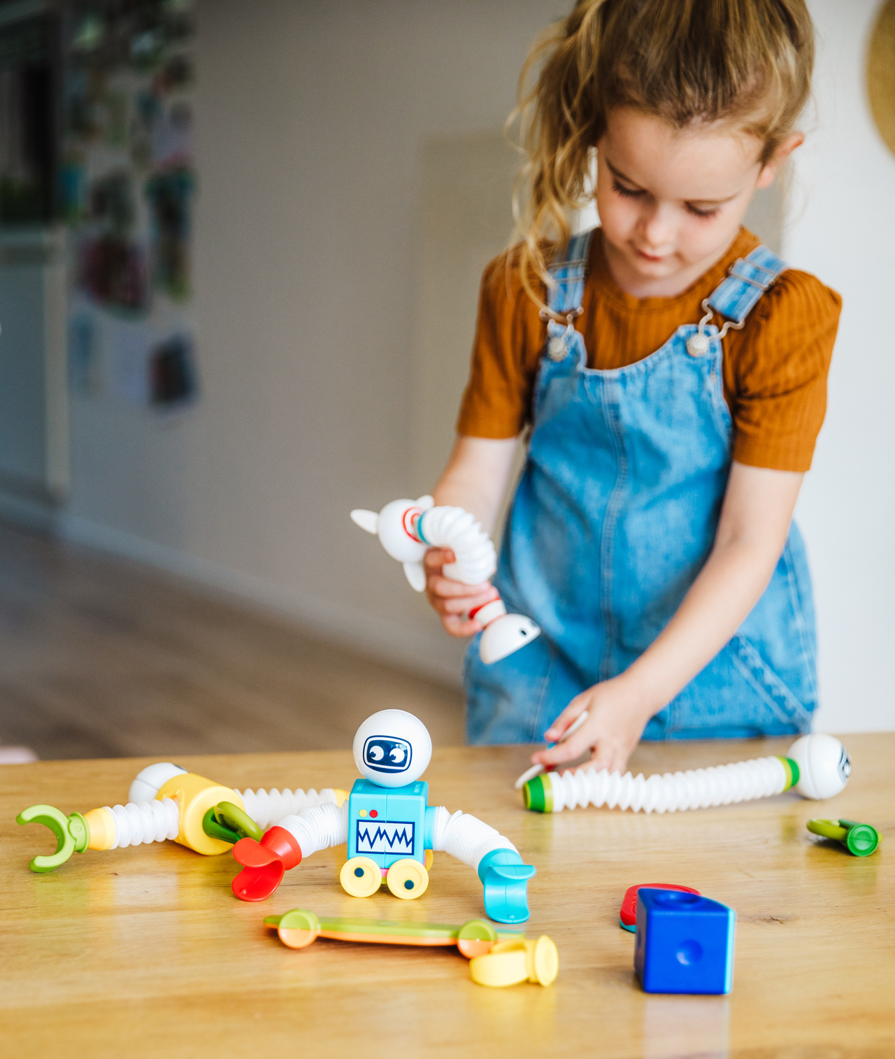 Ragazza che gioca con un robot giocattolo su un tavolo di legno.