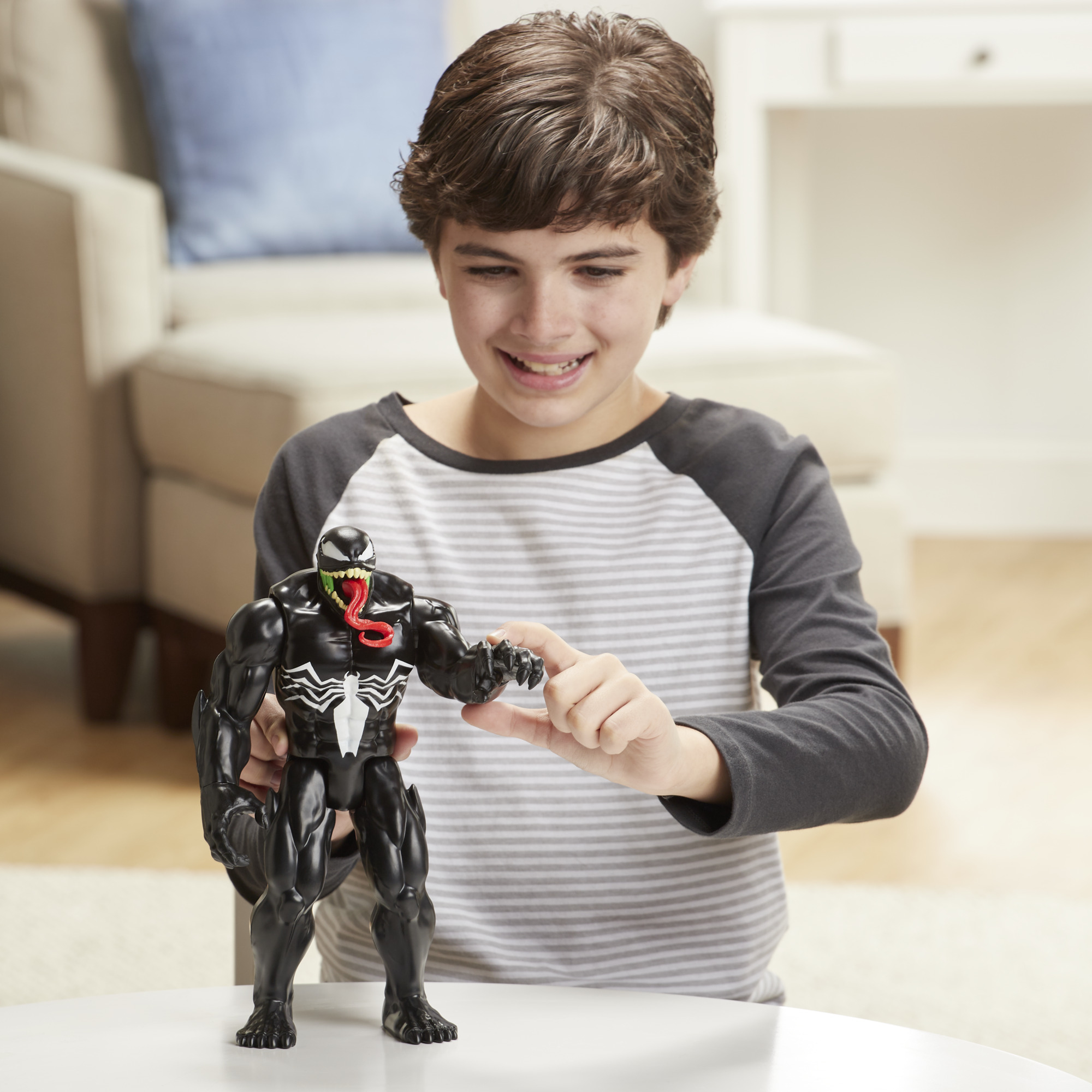 Un ragazzo sorride a un action figure nera di Venom. La figura è in posa con una mano tesa, come per afferrare.