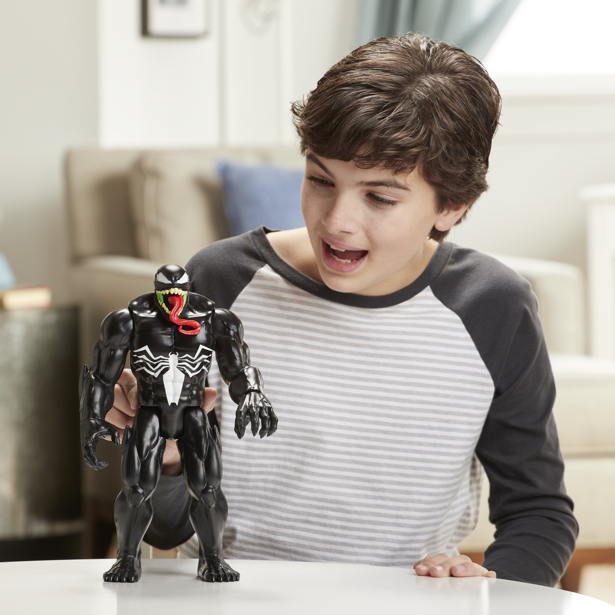 Ragazzo che guarda un action figure di Venom. Tavolo bianco e sfondo casa visibili.