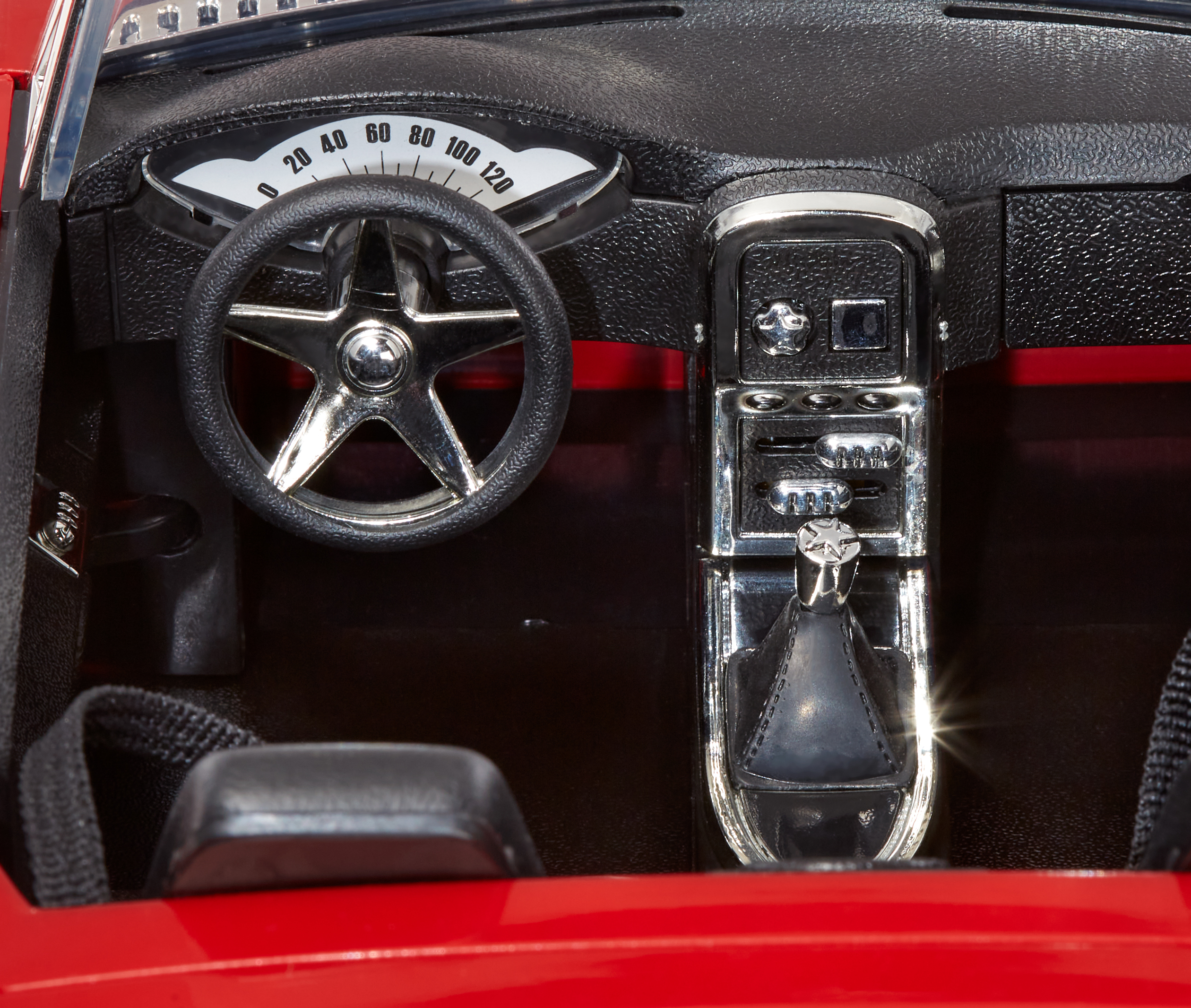 Zbliżenie na deskę rozdzielczą czerwonego samochodu, pokazujące kierownicę, wskaźniki i konsolę centralną.