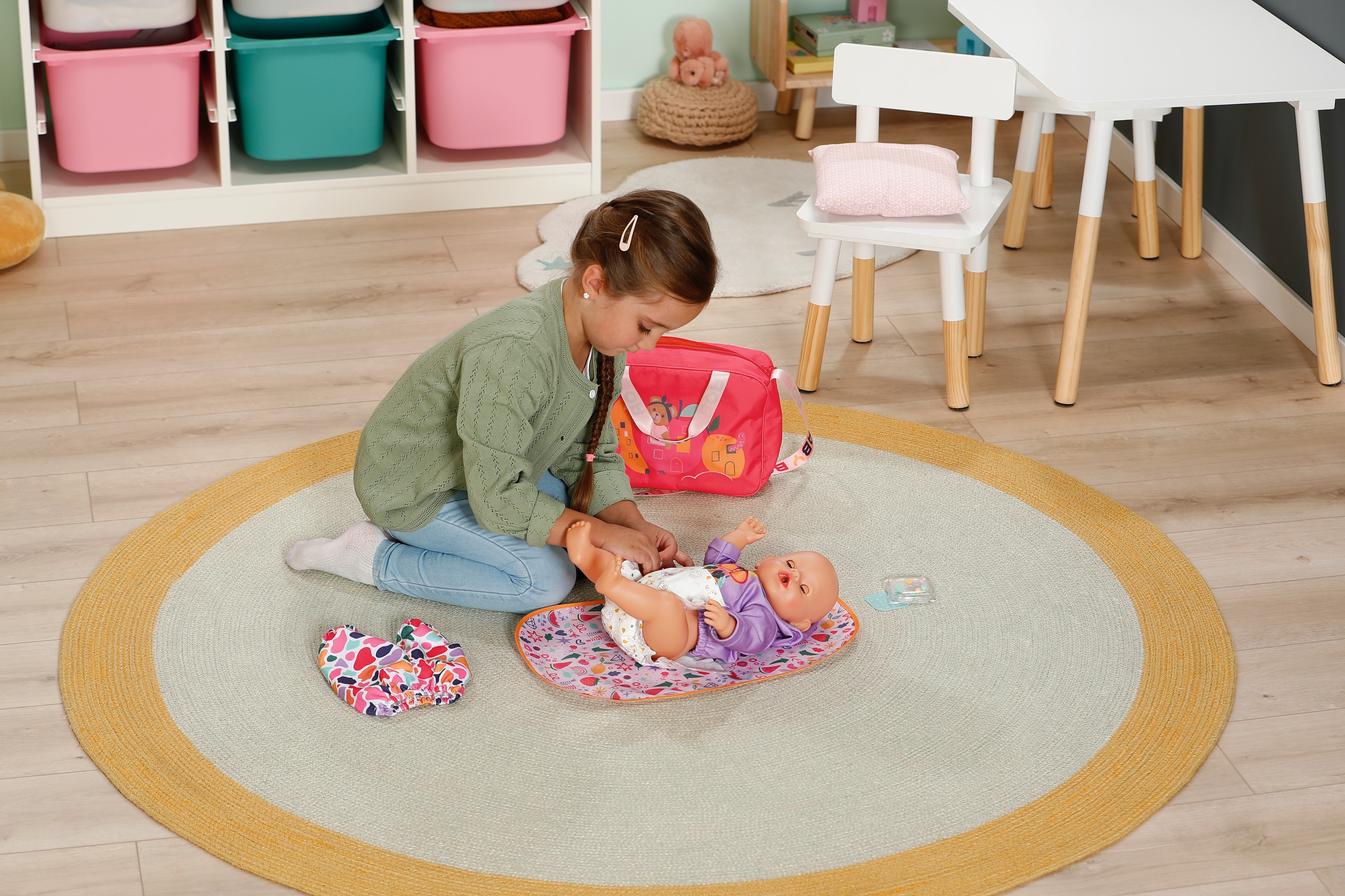 Dziewczynka bawiąca się lalką na dywanie z torbą na lalkę i akcesoriami. Wnętrze.